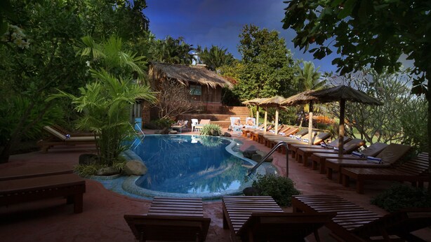 A pool area with lounge chairs and a thatched-roof structure. - Pride Sun Village Resort & Spa (Arpora)