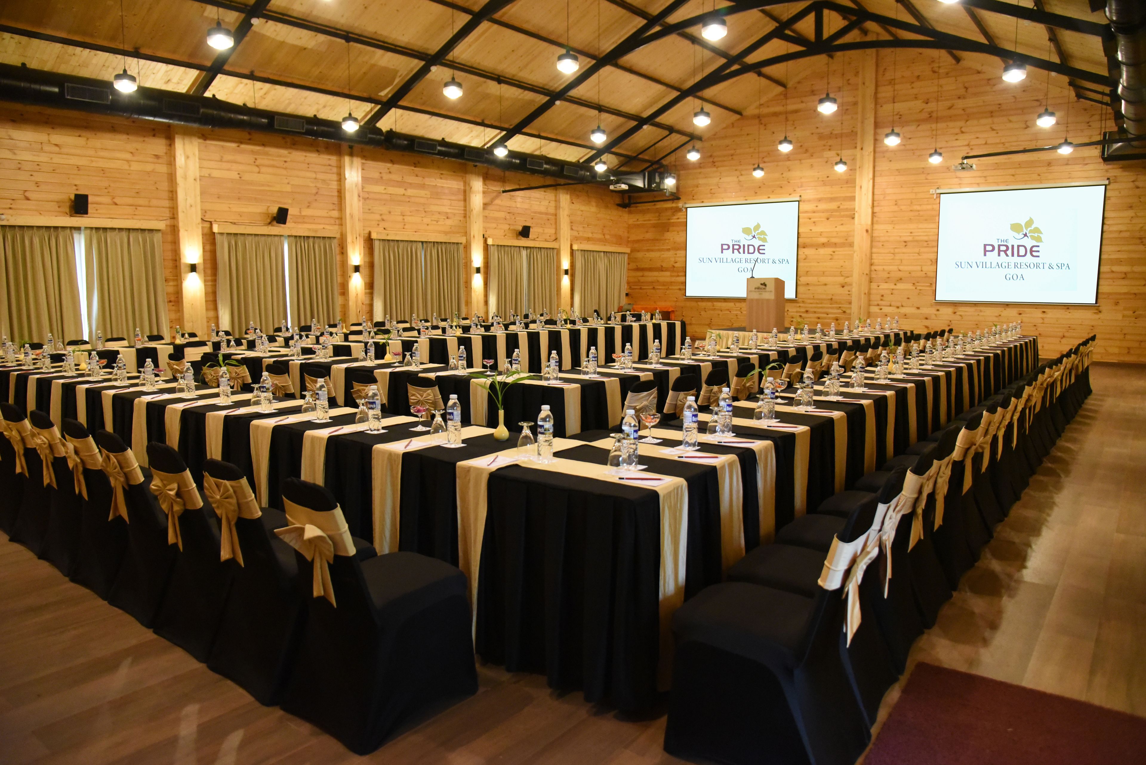 A conference room with rows of tables, black tablecloths, and gold sashes.
