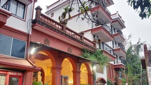 A multi-story building with a red and white facade, featuring a central arched entrance with potted plants, and balconies on the upper floors. - Pride Sun Village Resort & Spa (Arpora)