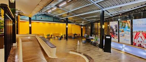 Un hall d’entrée spacieux avec un comptoir d’accueil incurvé, un plafond haut avec des poutres apparentes et un espace détente comprenant des chaises et des tables.