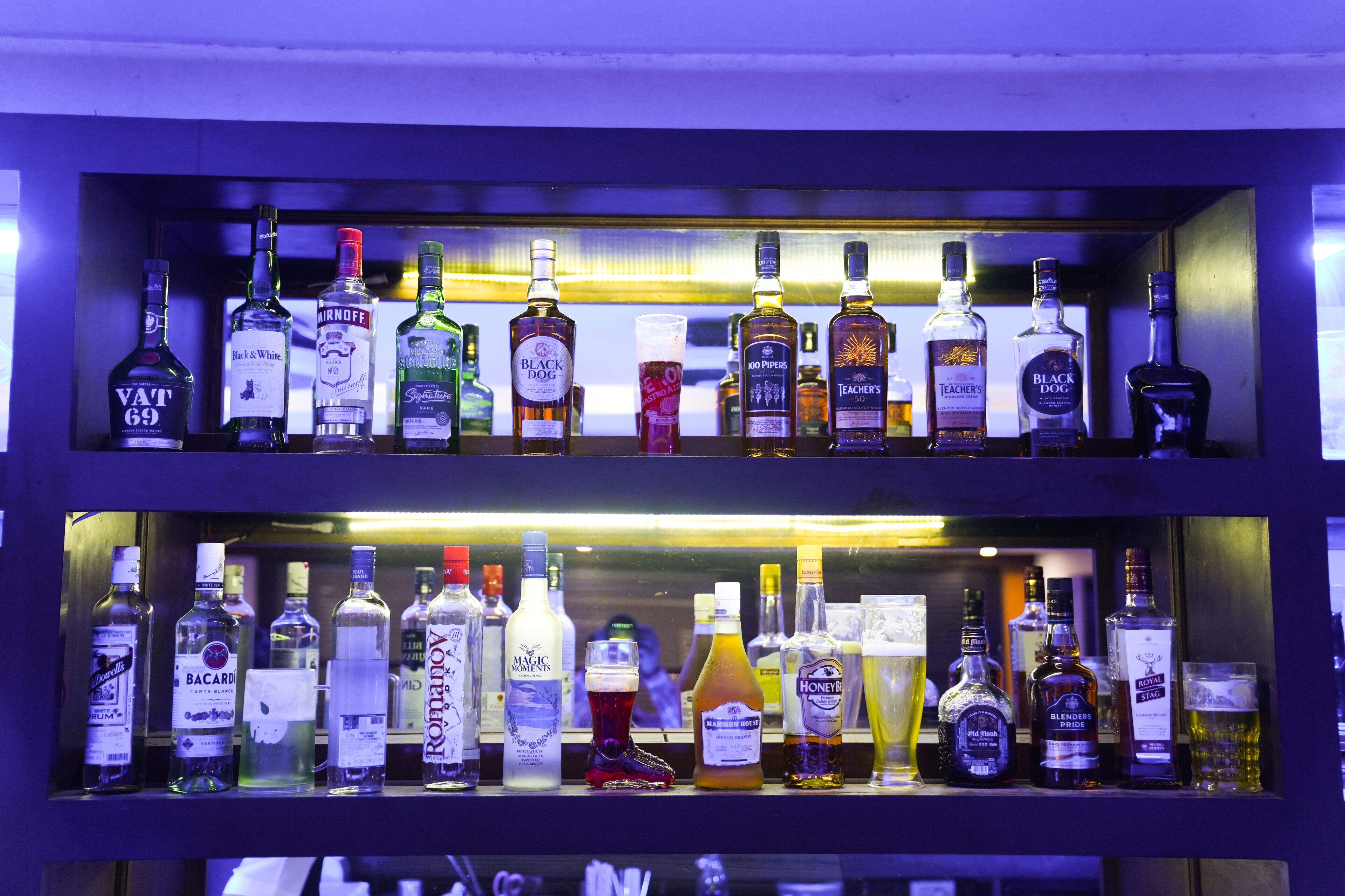 Deux étagères remplies de bouteilles et de verres de différentes sortes d’alcools.