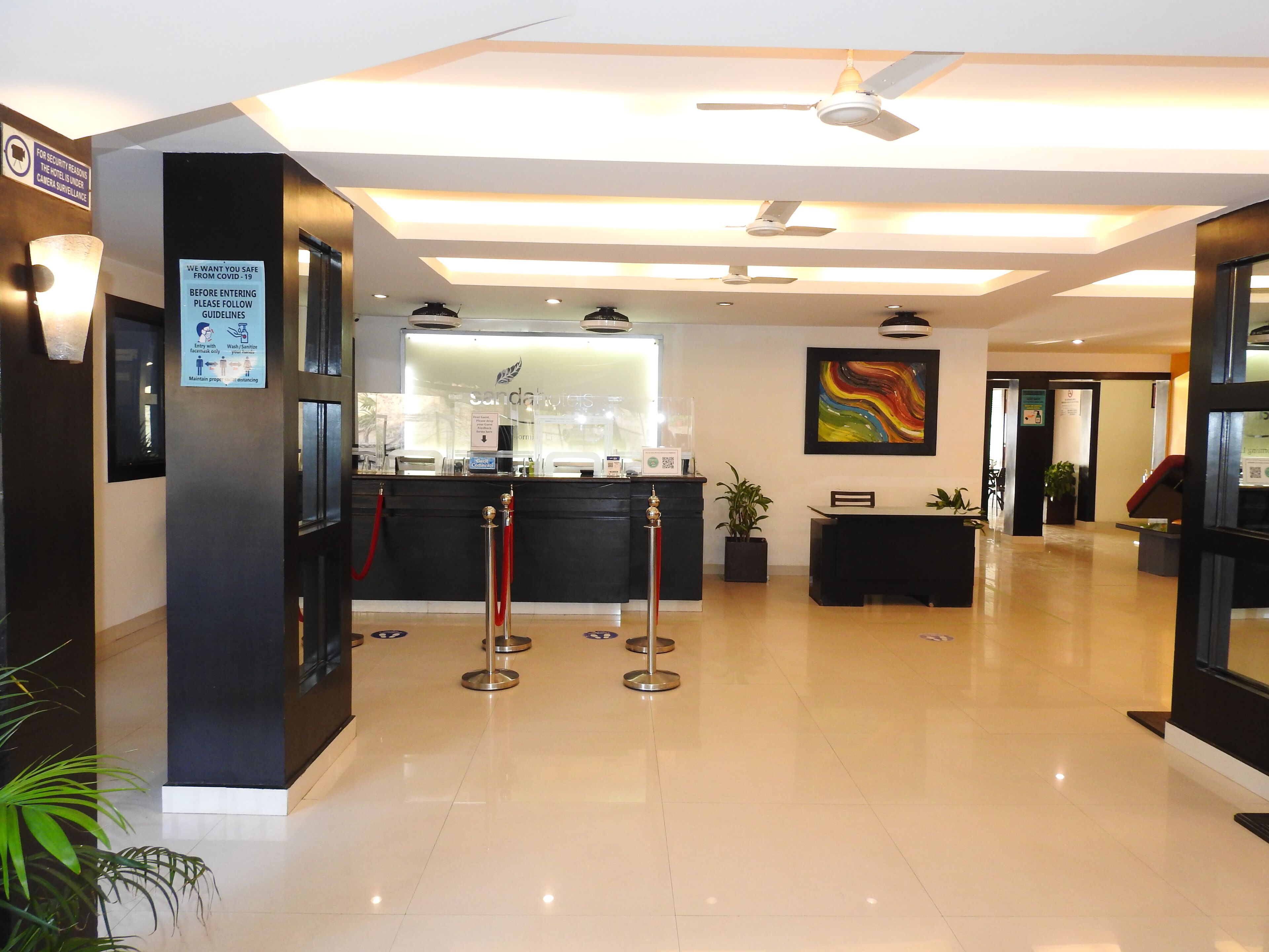 A hotel lobby with a reception desk, a waiting area, and a ceiling fan.