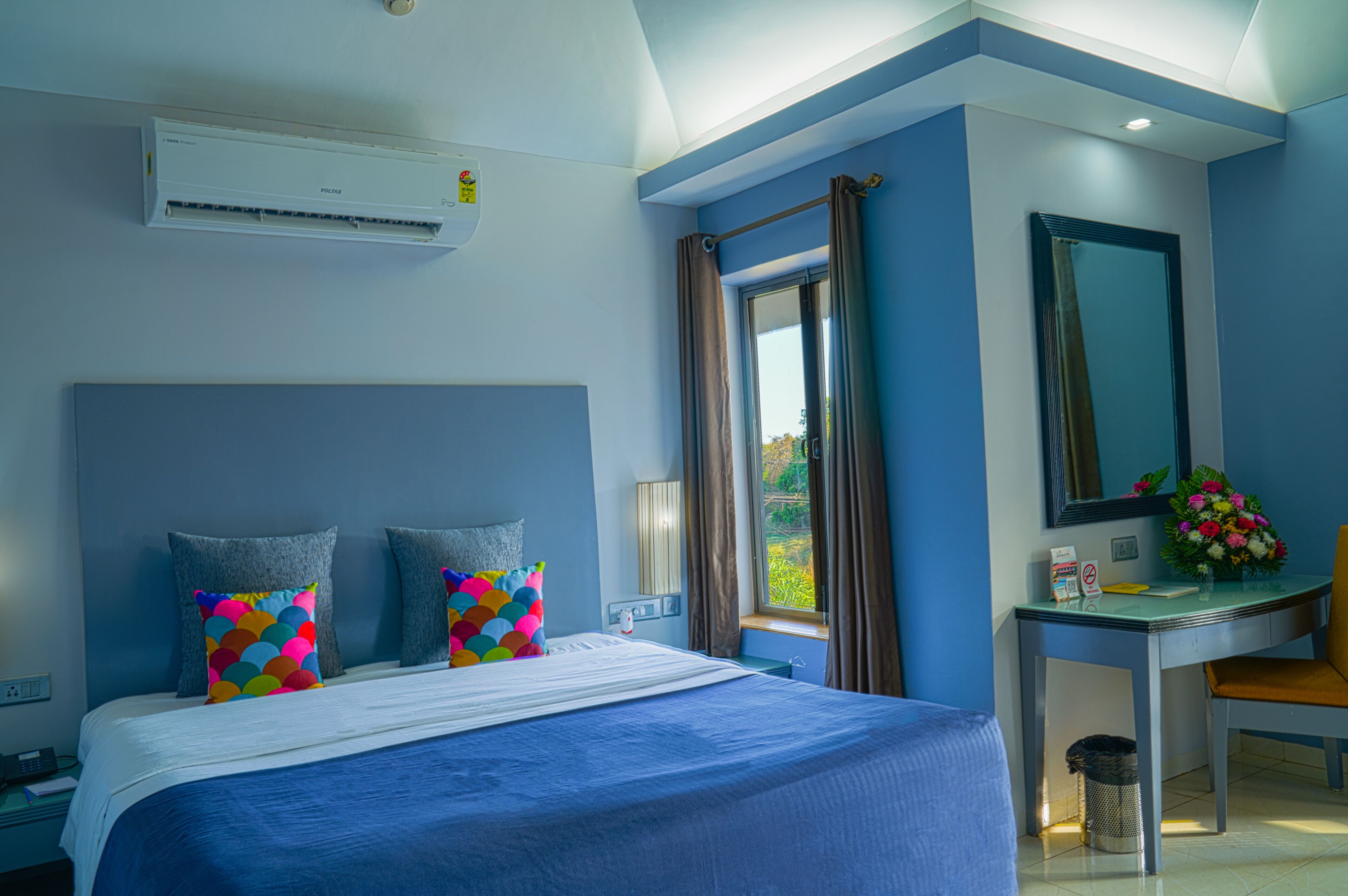 Quarto de hotel com cama, escrivaninha e janela.