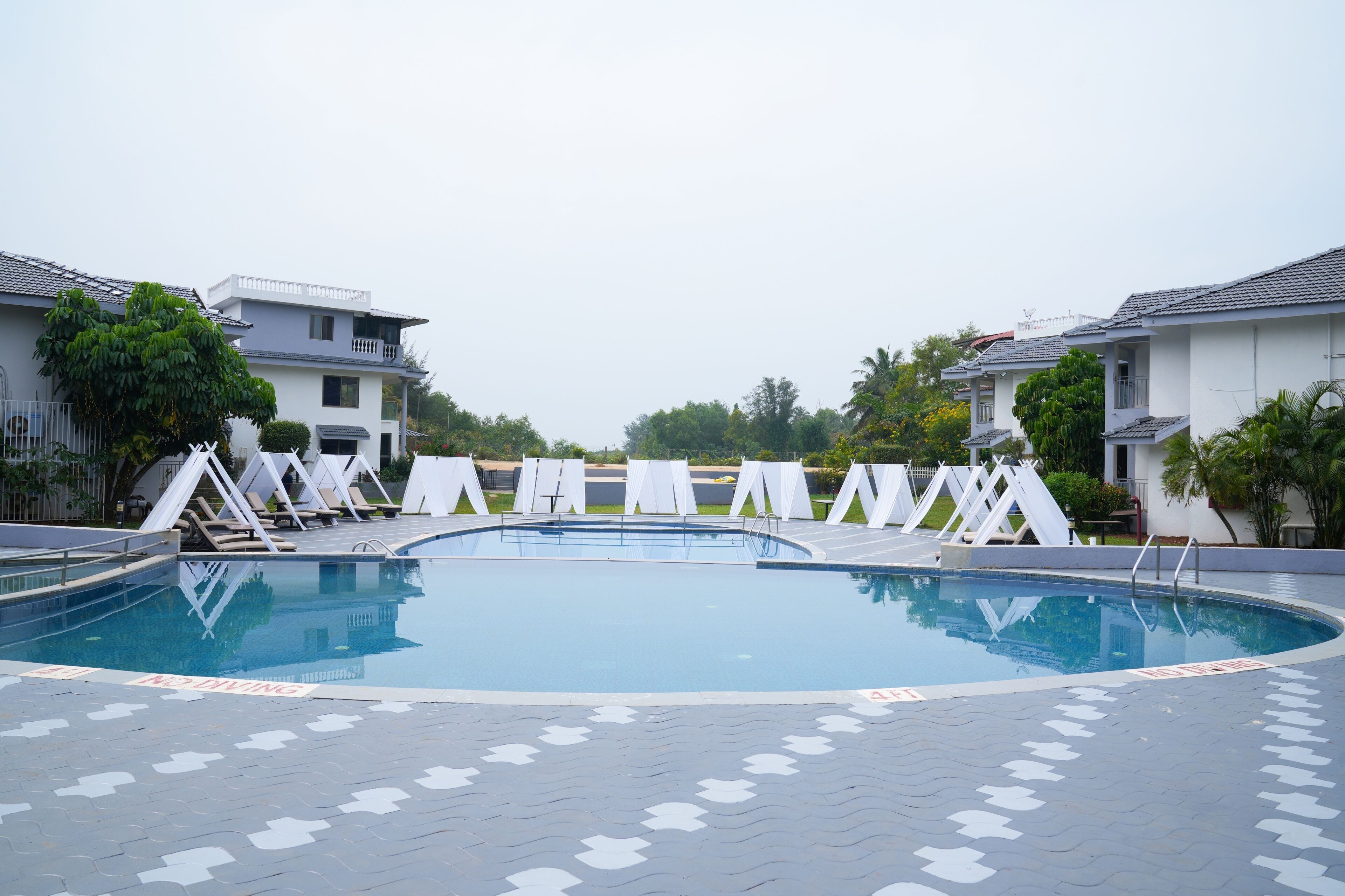 A swimming pool with a tiled deck, surrounded by white lounge chairs and a white fence.