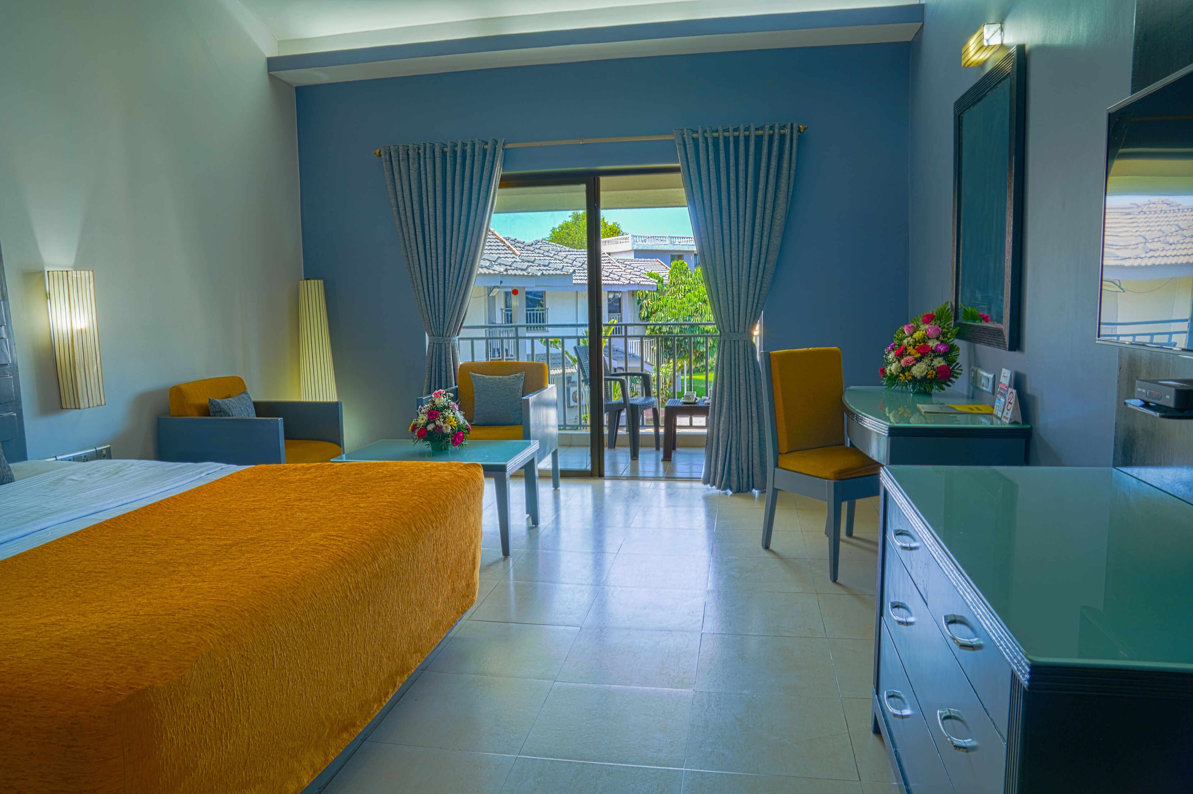 A hotel room with a bed, a desk, a chair, a dresser, and a balcony with curtains.