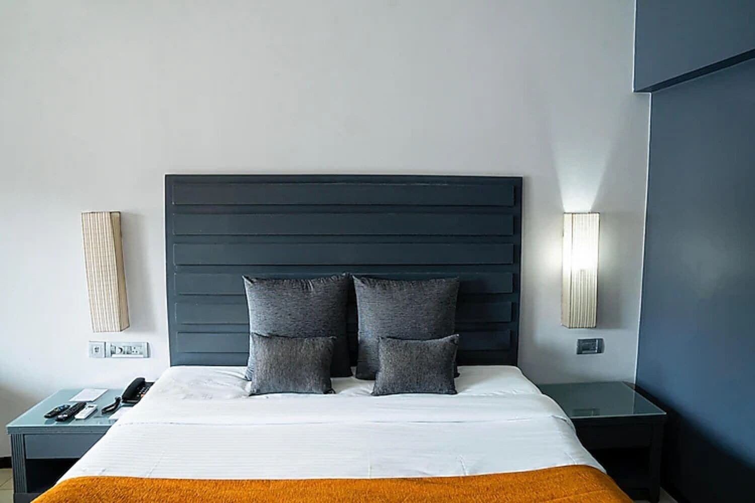 A hotel room with a large bed, two bedside tables, a nightstand, and a modern headboard.