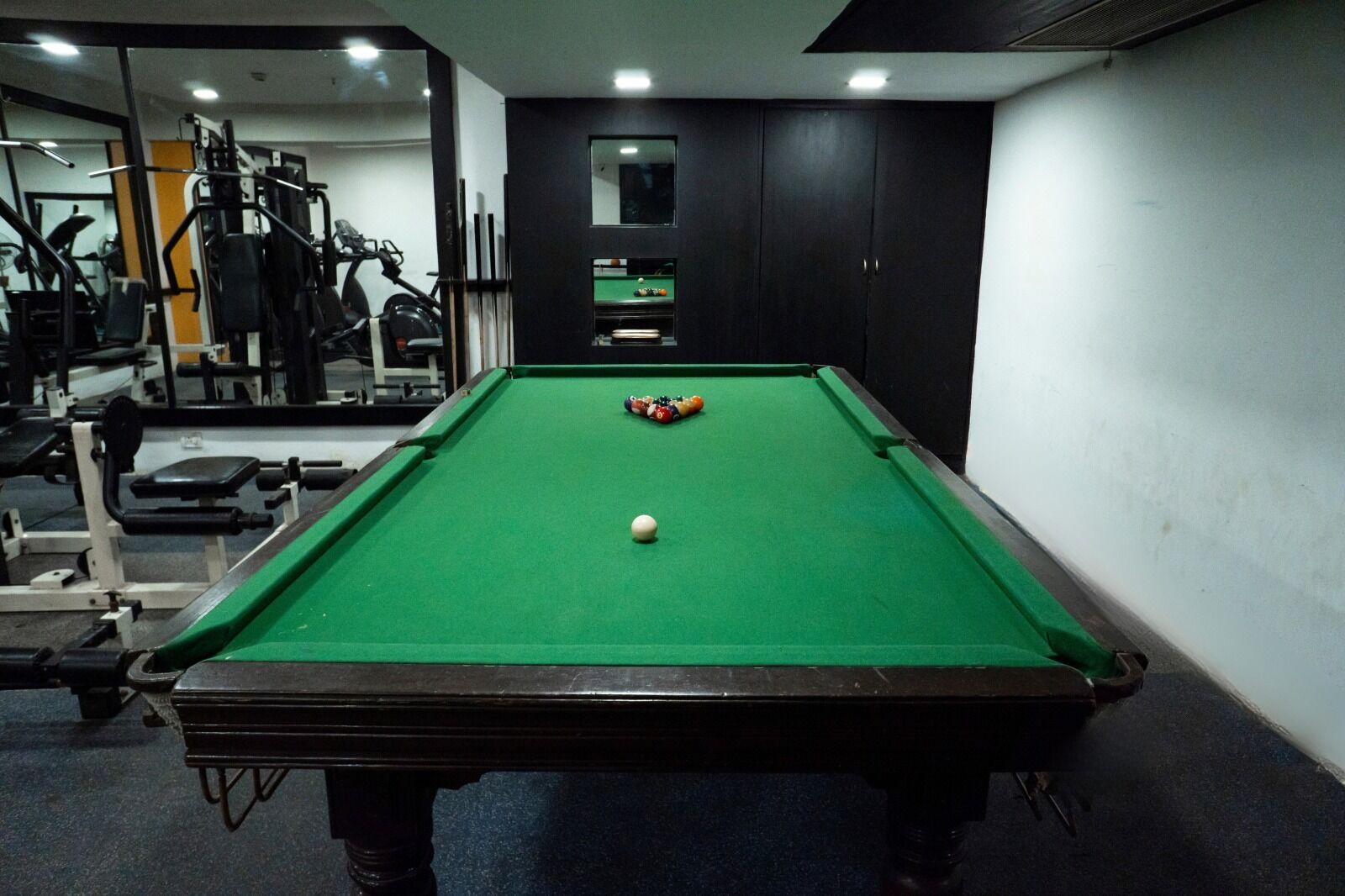 Een biljarttafel met ballen, een spiegel en fitnessapparatuur op de achtergrond.