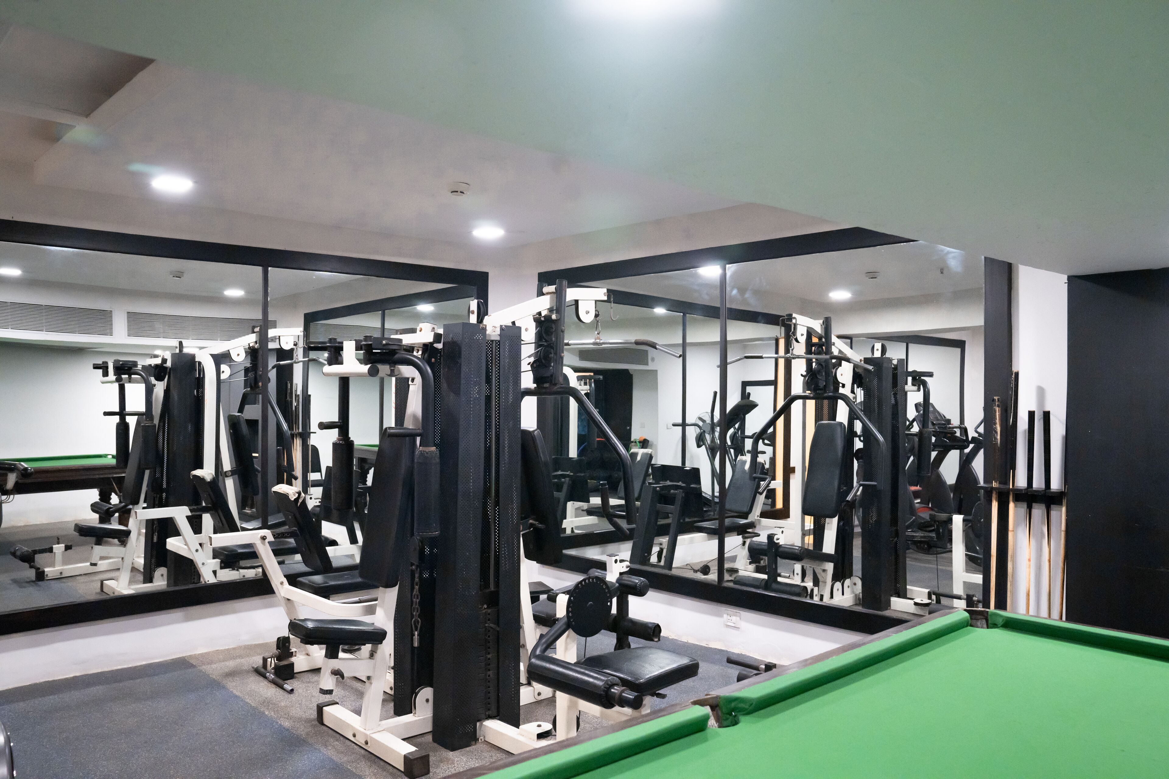 A gym with various exercise machines, mirrors, and a green pool table.