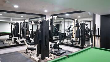 Un gimnasio con diversas máquinas de ejercicio, espejos y una mesa de billar verde.