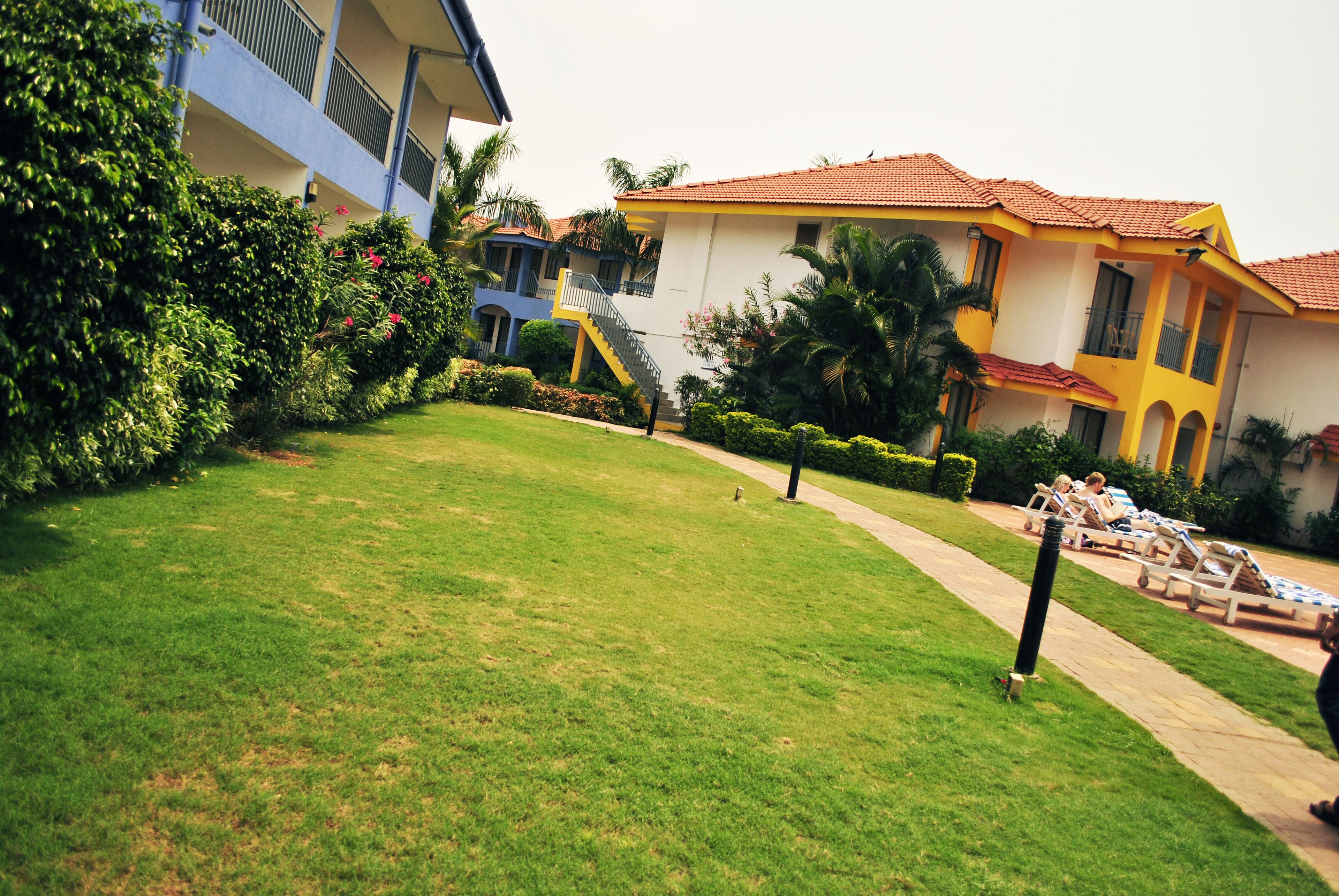 A hotel with a well-maintained lawn, a pool area with lounge chairs, and a two-story building with balconies.