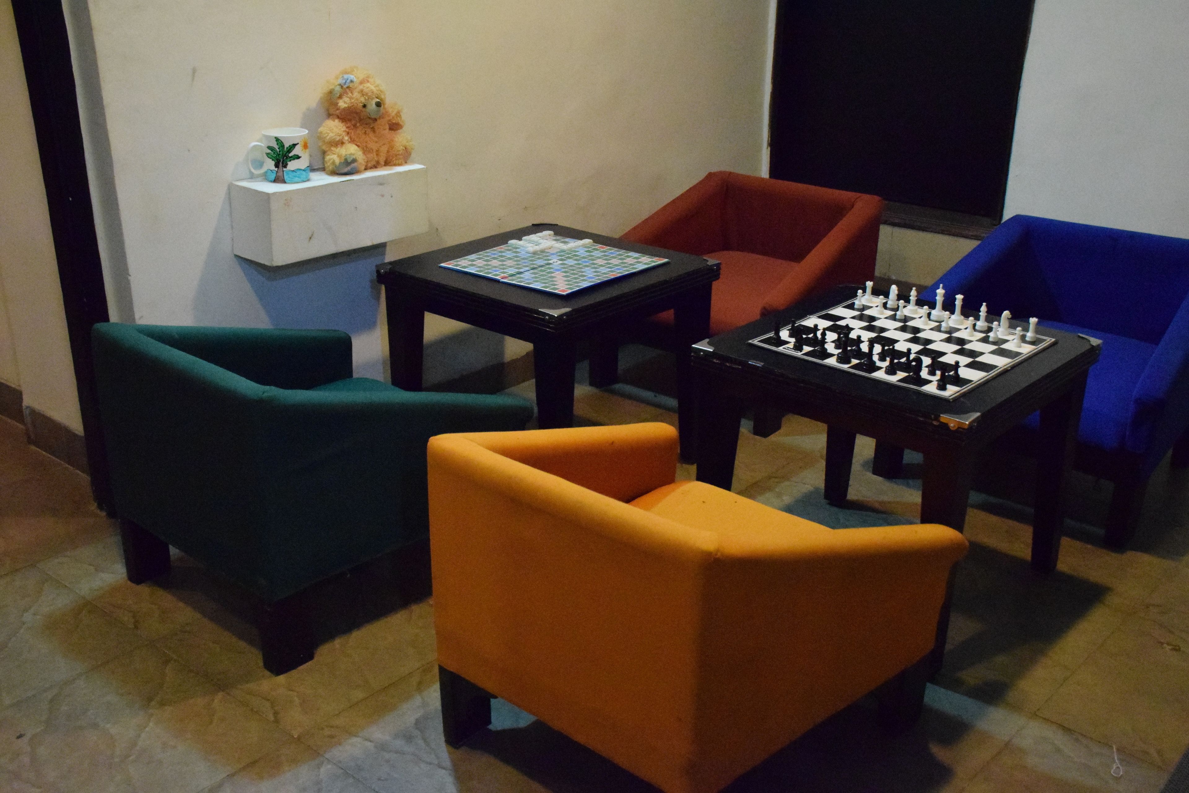 Una habitación con un tablero de ajedrez, un osito de peluche y una pequeña planta de palma sobre una estantería.