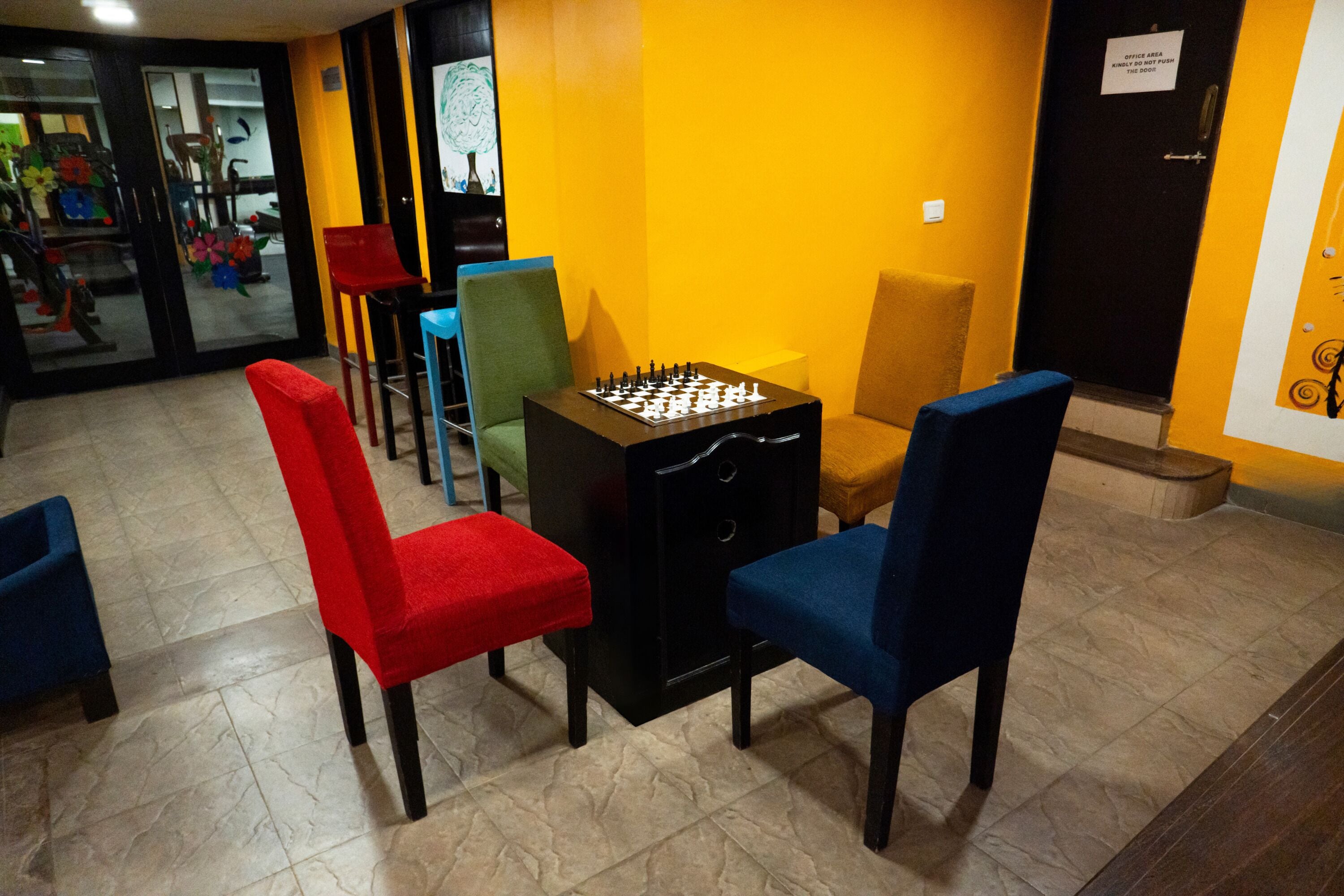 A room with a foosball table, colorful chairs, and a yellow wall.