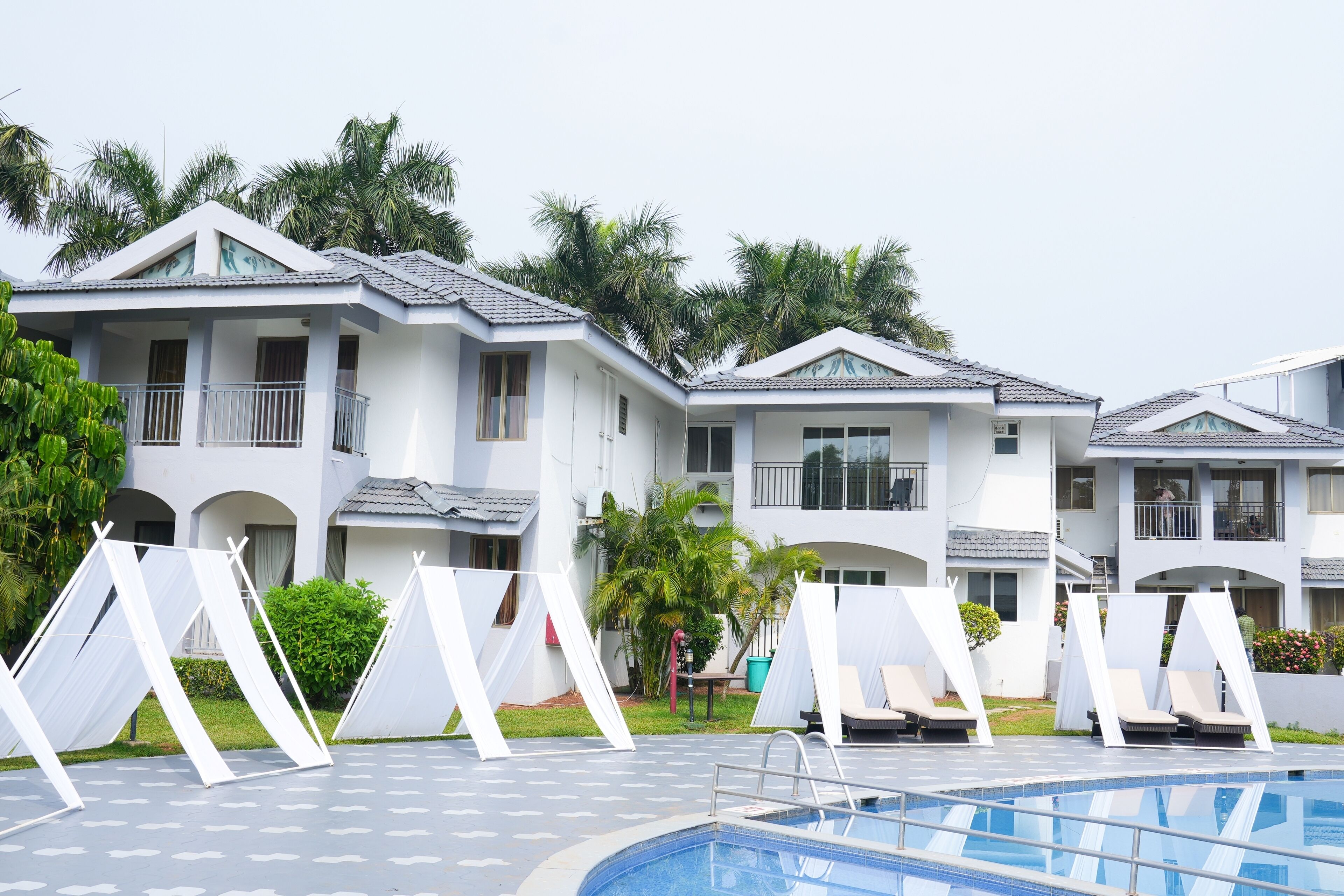 A hotel with multiple white buildings, a swimming pool, and white canopies over the pool area.