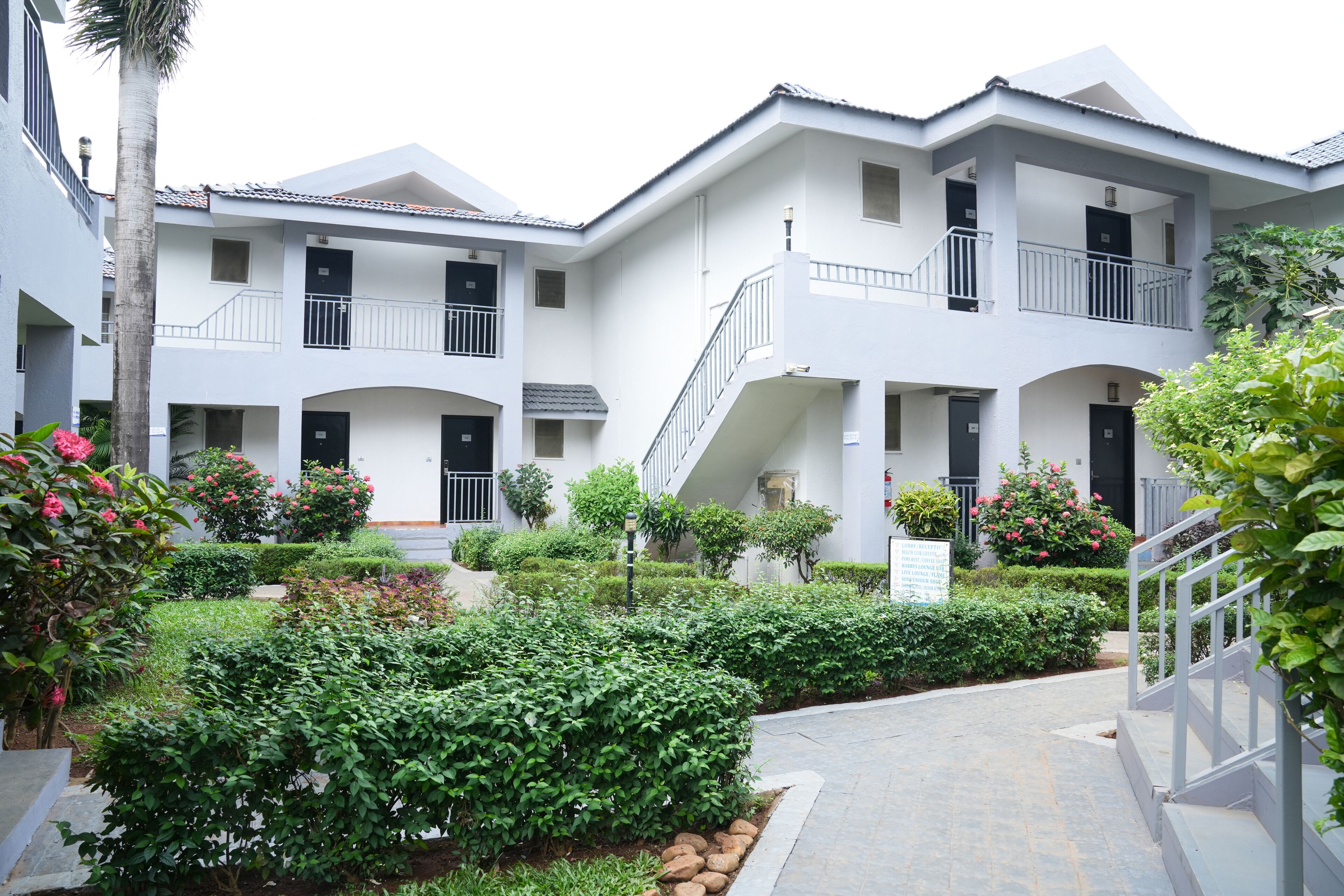 A multi-story building with balconies, a central courtyard with greenery, and a pathway leading to the entrance.