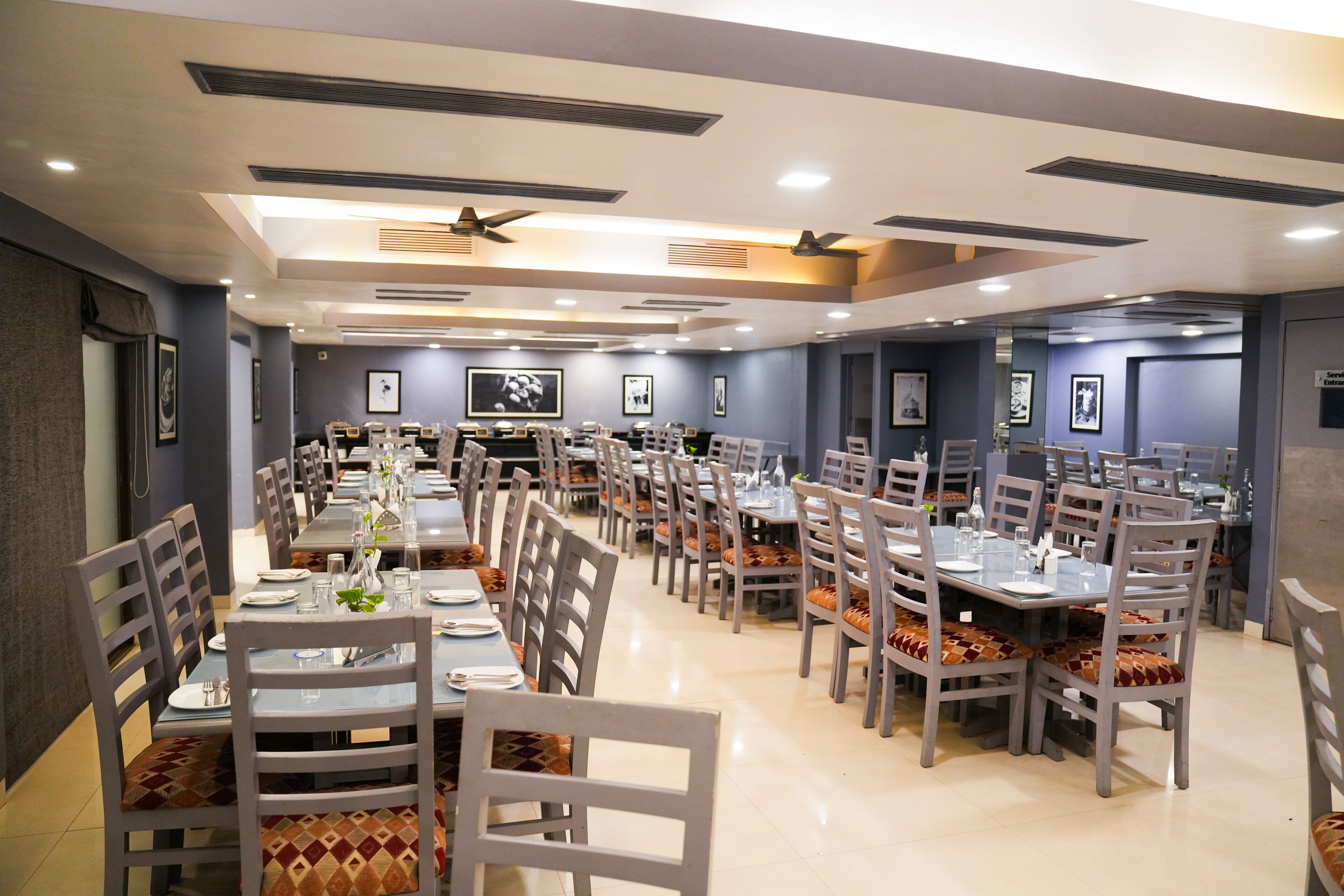 A spacious dining area with multiple tables and chairs, ceiling fans, and framed pictures on the walls.