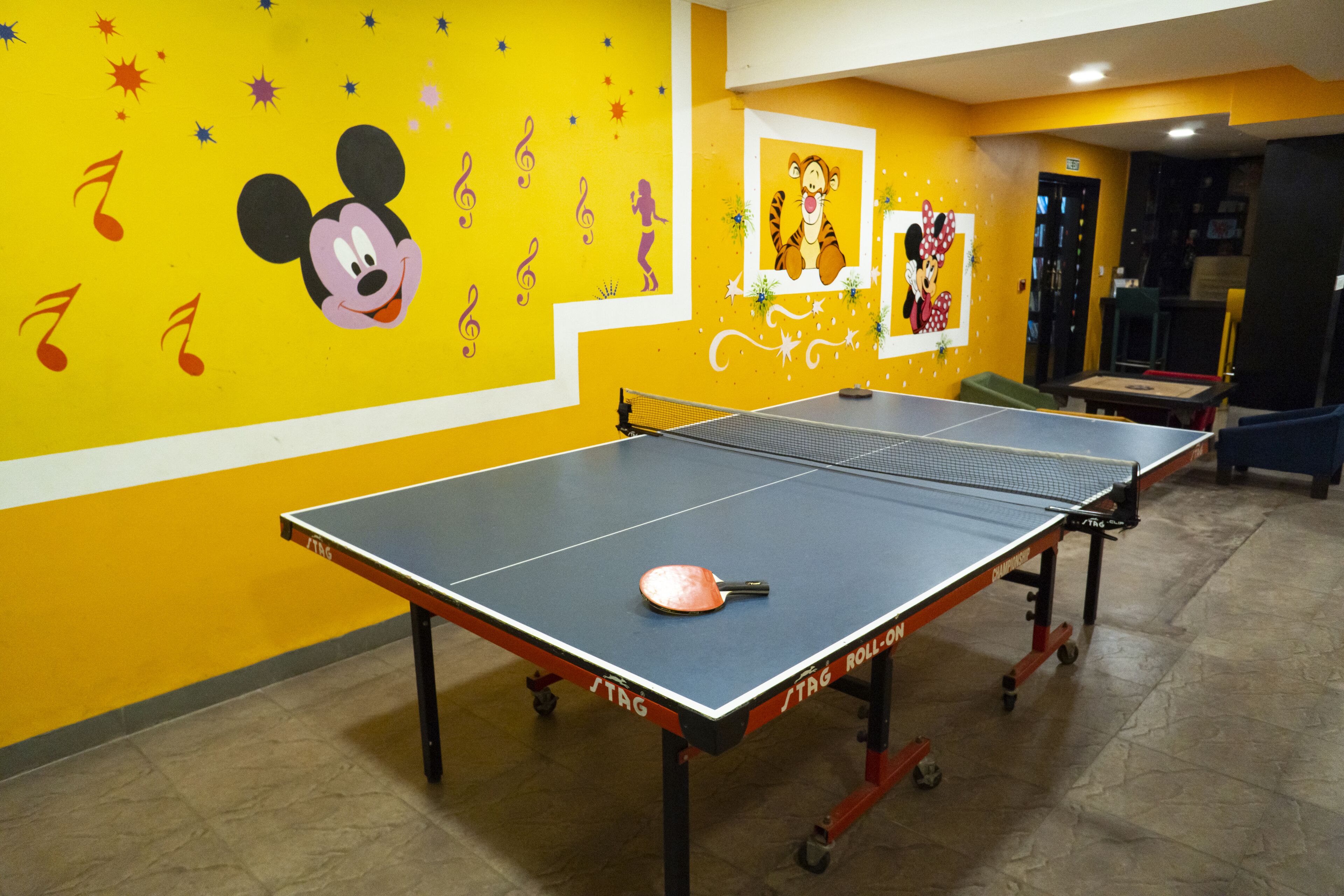 A ping pong table in a room with yellow walls, decorated with Mickey Mouse and a tiger.