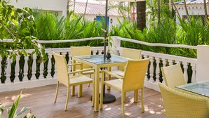 Un patio al aire libre con mobiliario de mimbre amarillo, sombrillas blancas y abundante vegetación.
