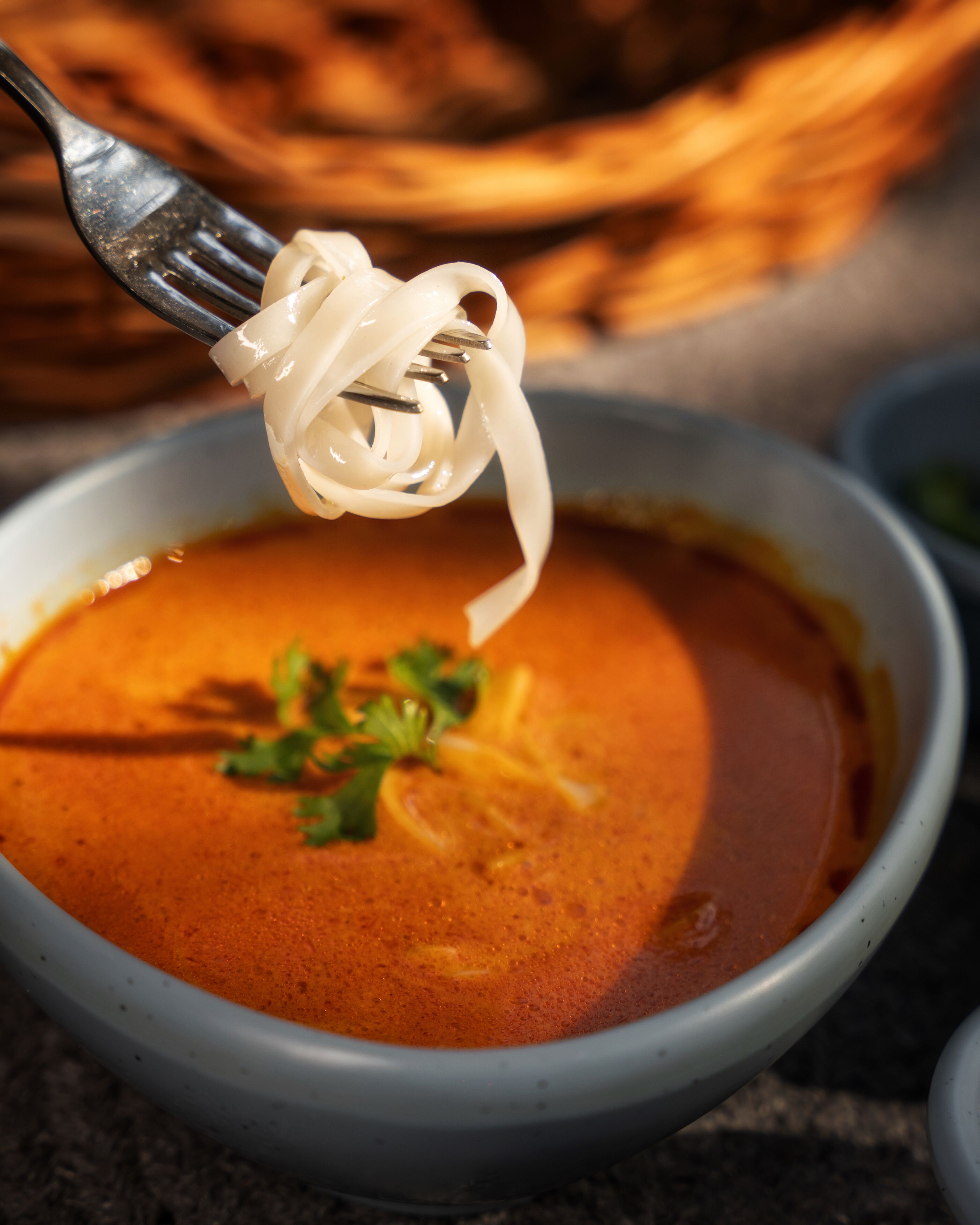A bowl of soup with noodles being lifted by a fork.