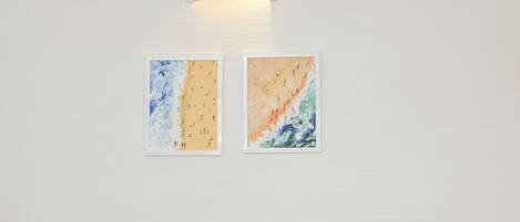 Una sala moderna con un sofá azul, cojines a rayas y una mesa de centro de cristal con fruta y una bebida. Dos obras de arte abstracto decoran la pared.