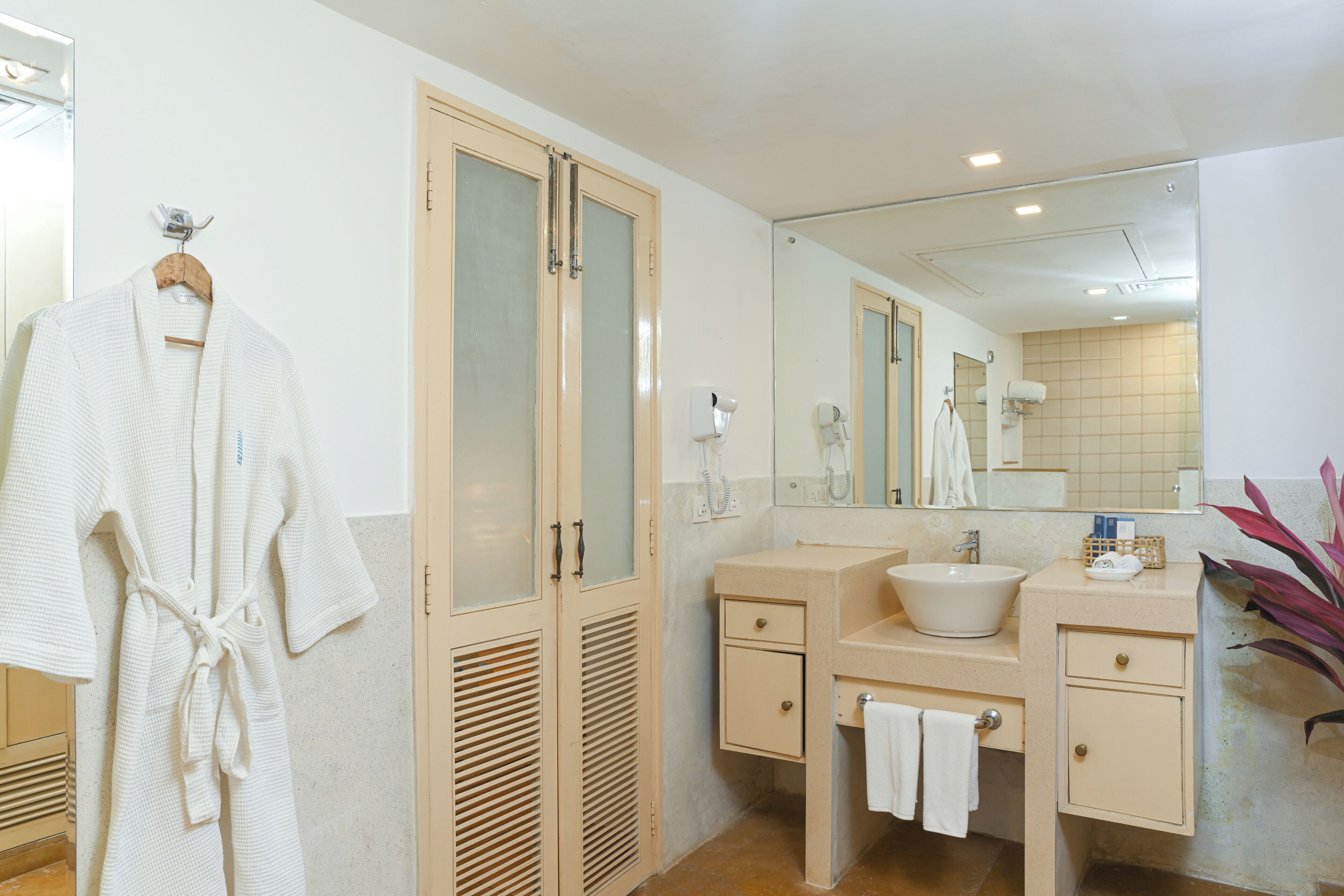 A bathroom with a large mirror, a sink, a robe hanging on a rack, and a towel rack.