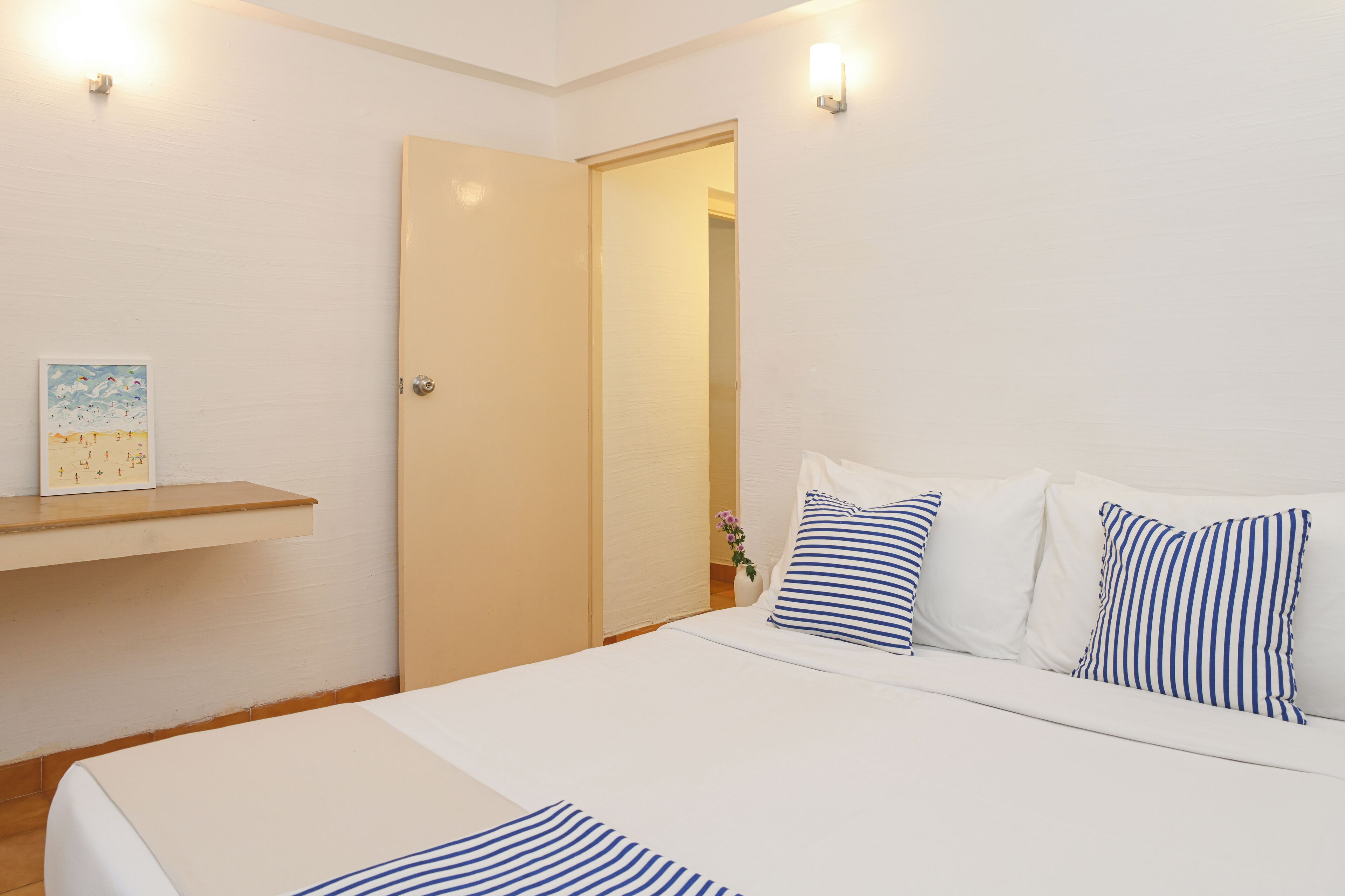 A neatly arranged bedroom with a bed, pillows, a nightstand, and a wall-mounted shelf.