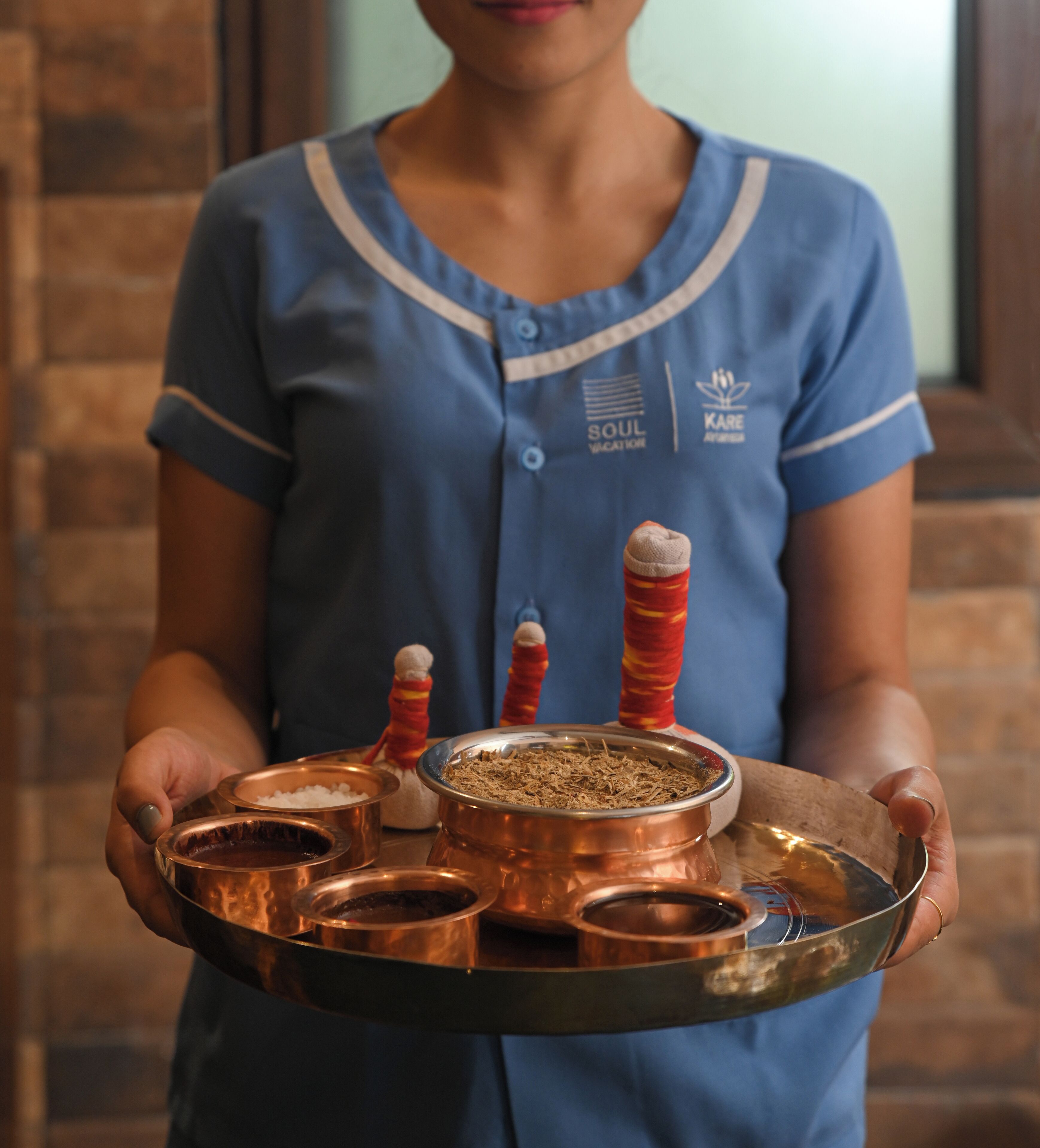 A person holding a tray with multiple copper containers, some with red and white striped handles.