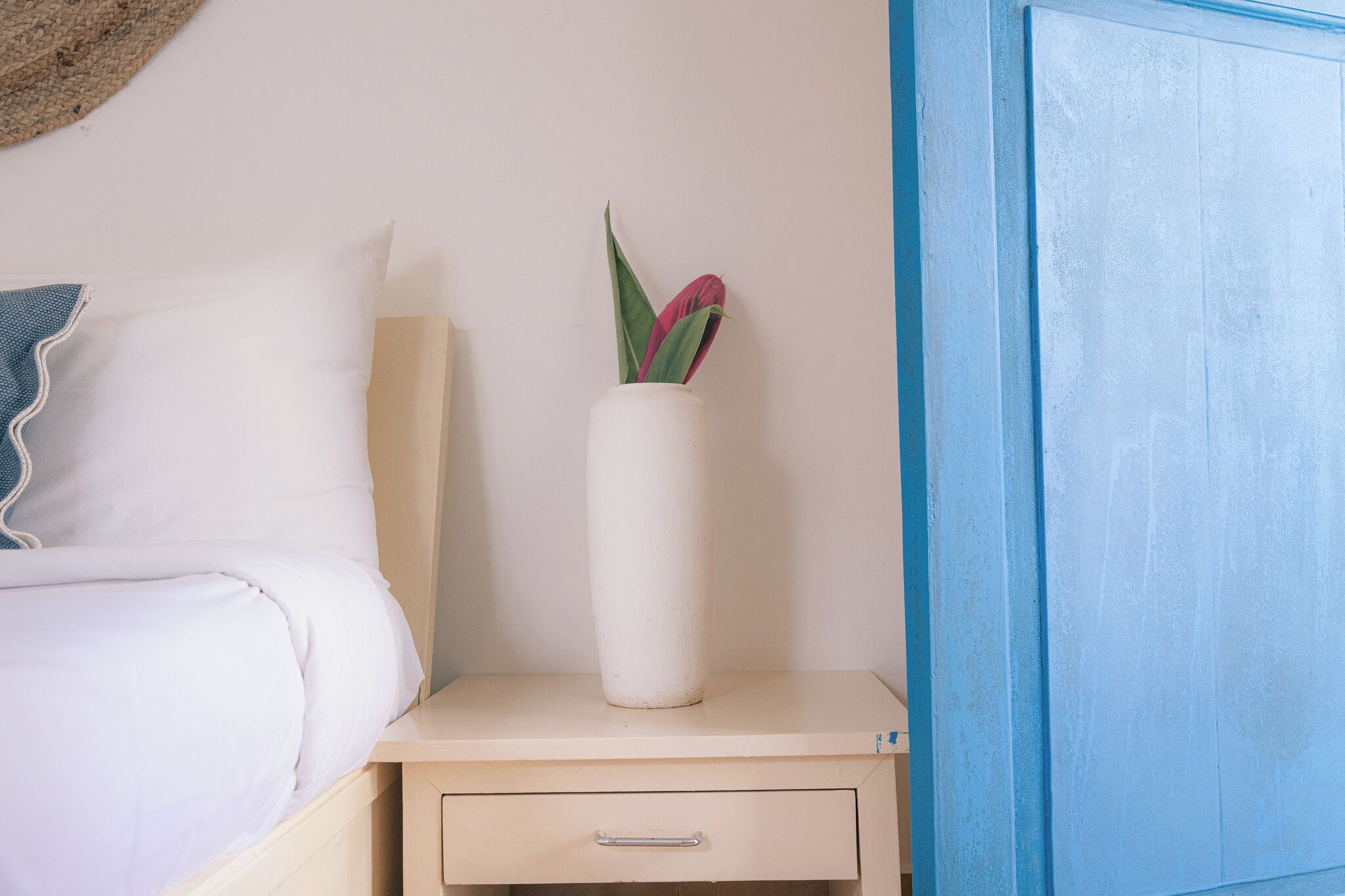 Quarto com uma cama, um criado-mudo com um vaso de flores e uma porta azul.