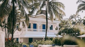 Un edificio blanco con detalles azules, rodeado de palmeras y una piscina.