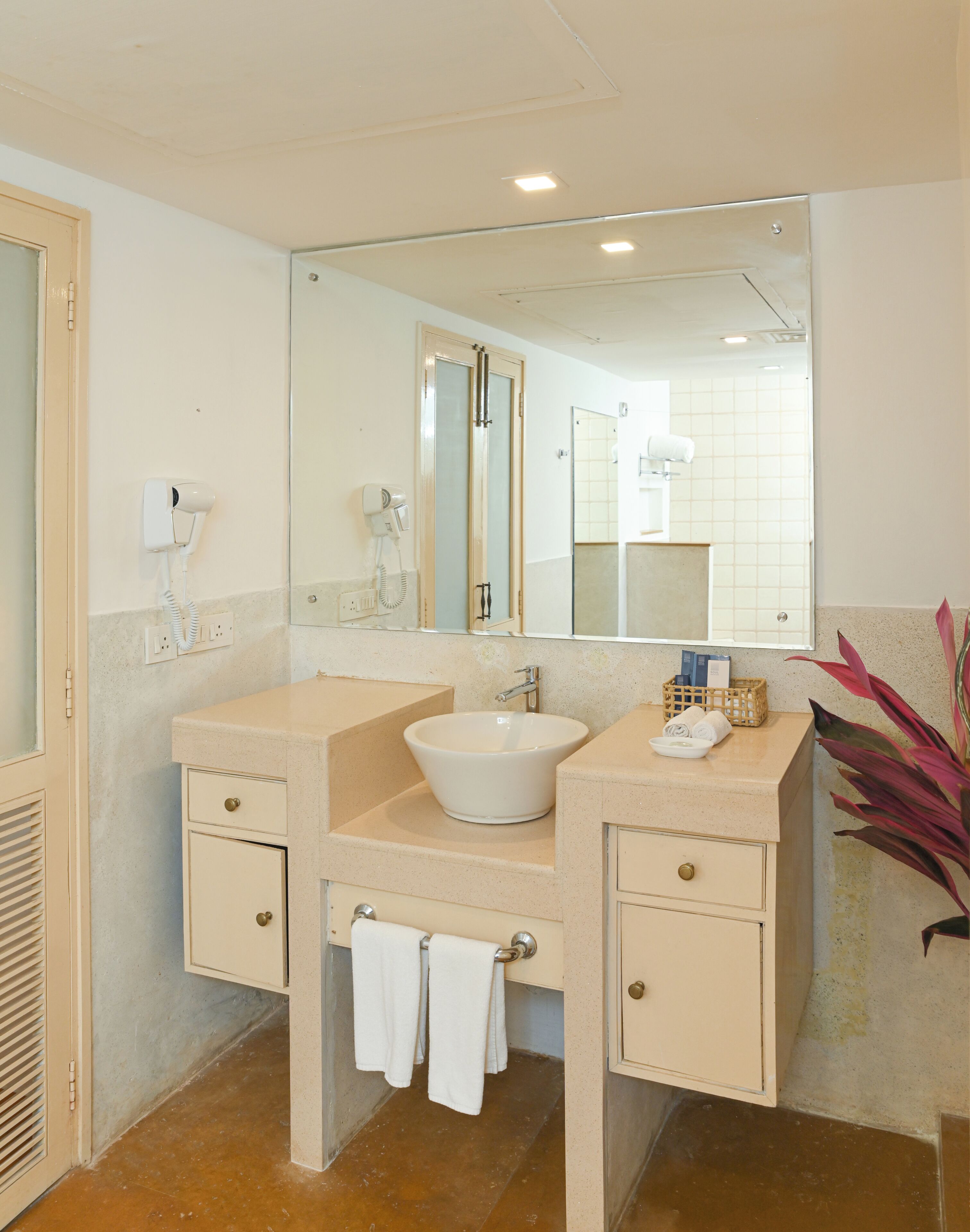 A bathroom with a white sink, two towel racks, a mirror, and a hairdryer on the wall.