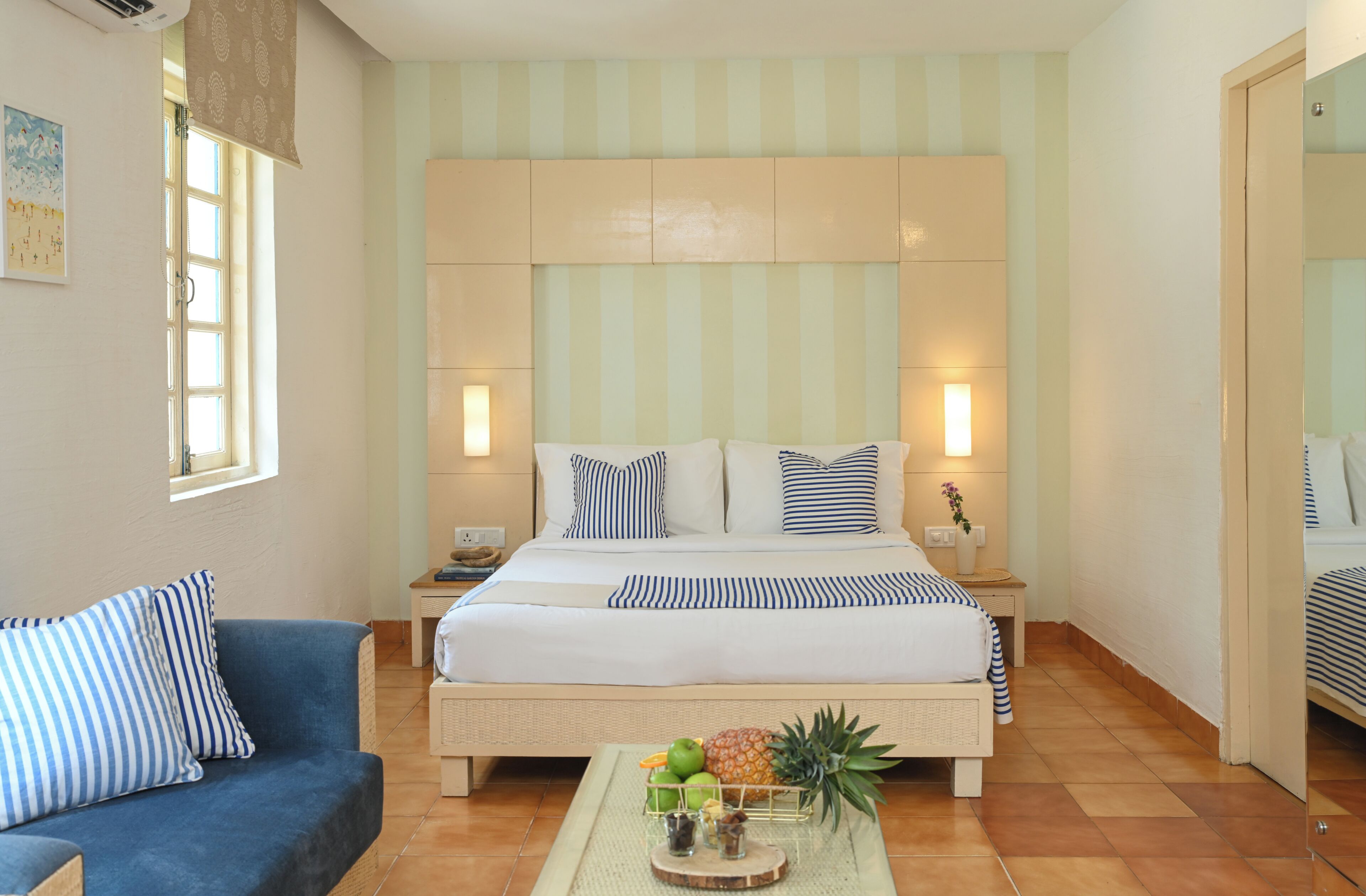 Un dormitorio con cama, mesitas de noche, un sofá azul y una bandeja de frutas en el suelo.