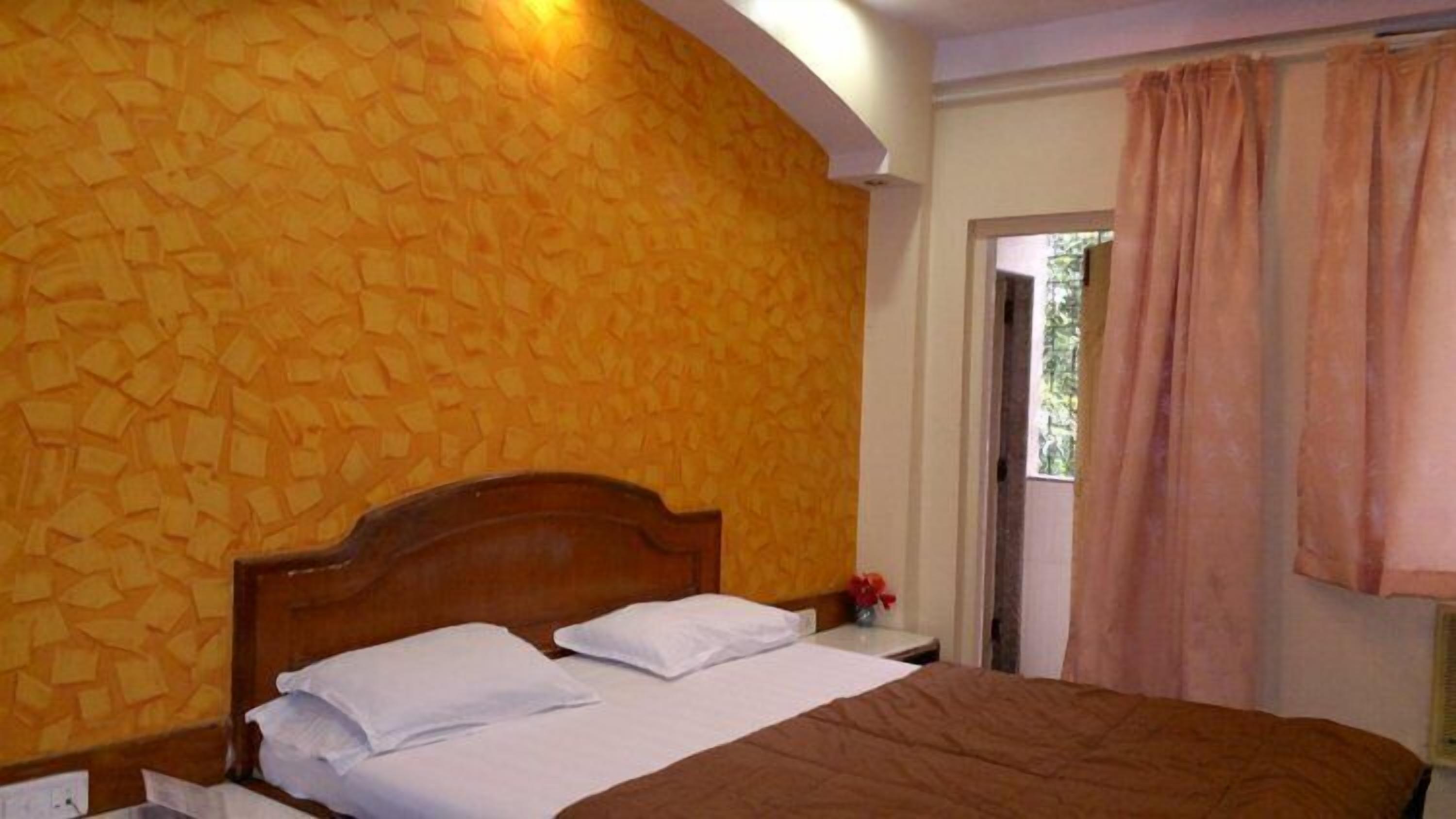Un dormitorio con cabecera de madera, cama con ropa de cama blanca y marrón, y pared amarilla con textura.
