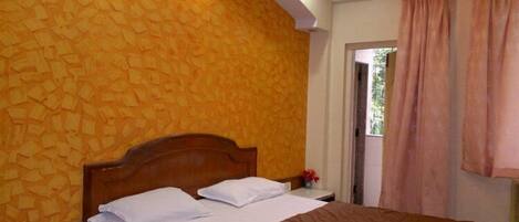 Un dormitorio con cabecera de madera, cama con ropa de cama blanca y marrón, y pared amarilla con textura.