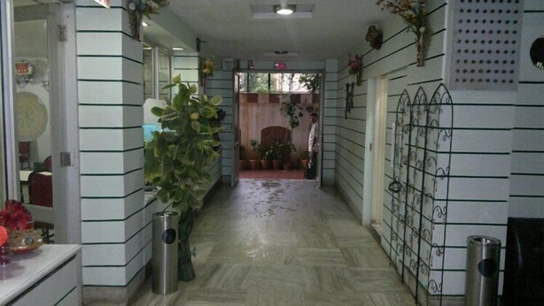 A hallway with tiled walls, a tiled floor, potted plants, and a metal gate on the right. - Hotel Sea Lord (Mumbai)