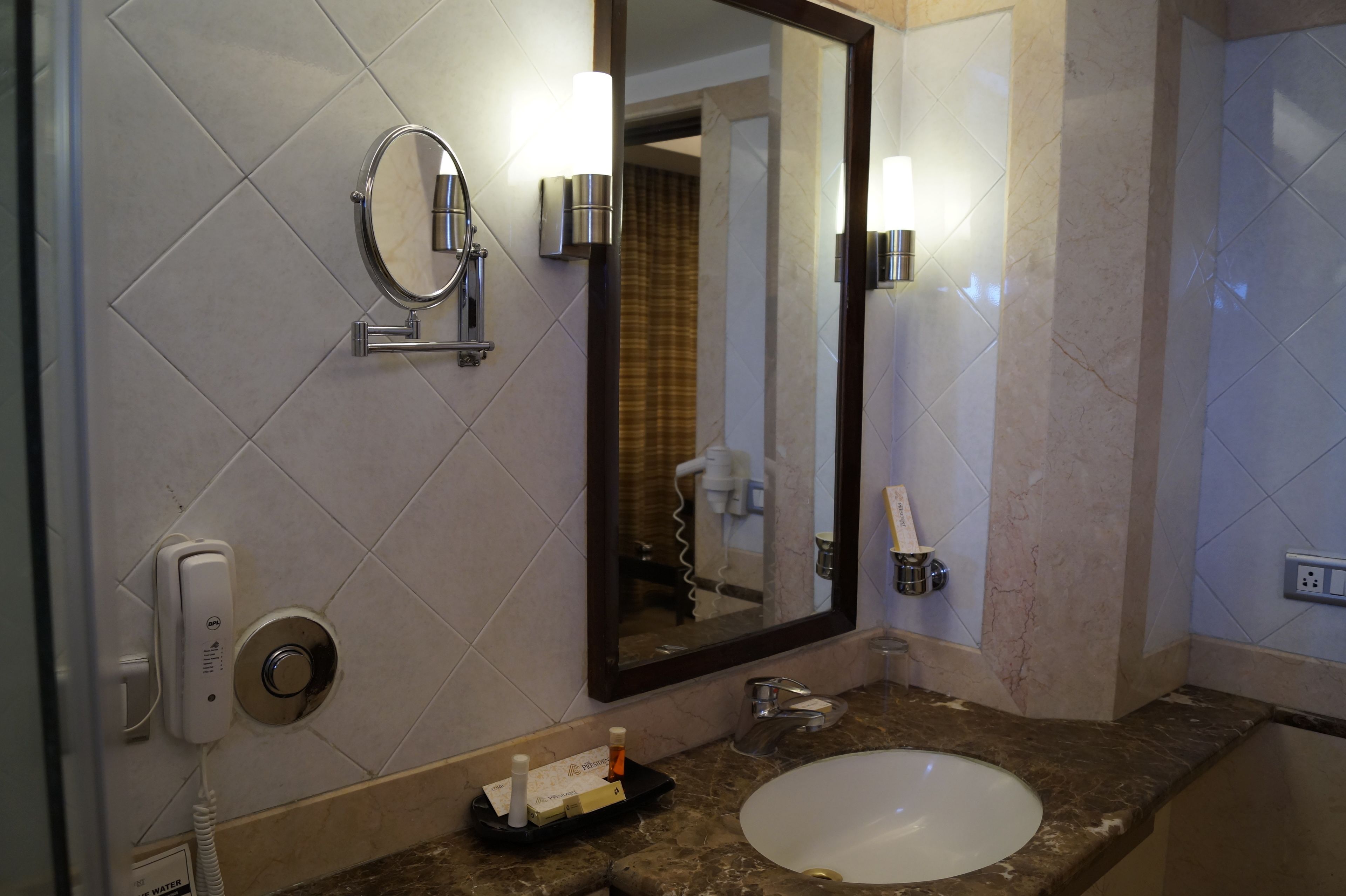 A bathroom with a white sink, a mirror, a towel rack, a handheld showerhead, and a toilet visible in the reflection.