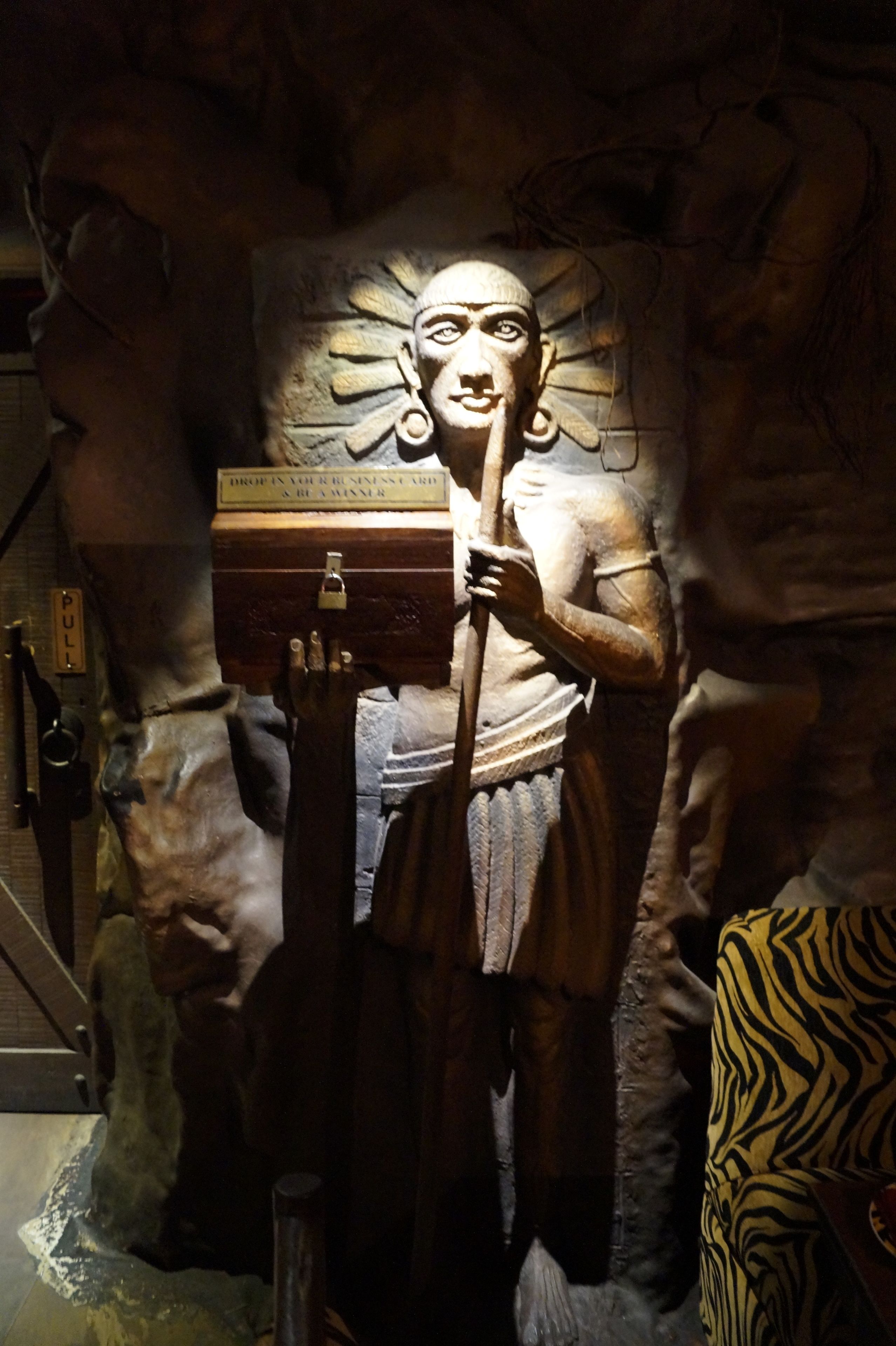 A statue of a figure holding a box, set against a cave-like backdrop with a sign reading "PULL".
