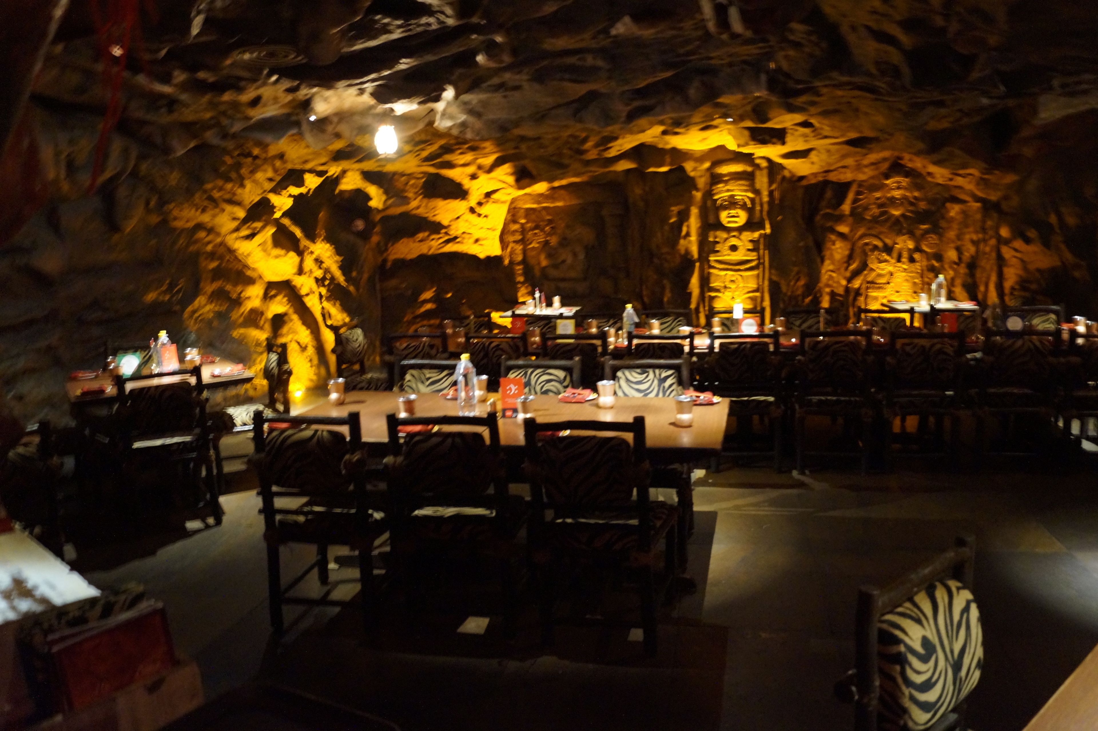 Um restaurante com interior tipo gruta, mesas montadas com velas e um pilar central.