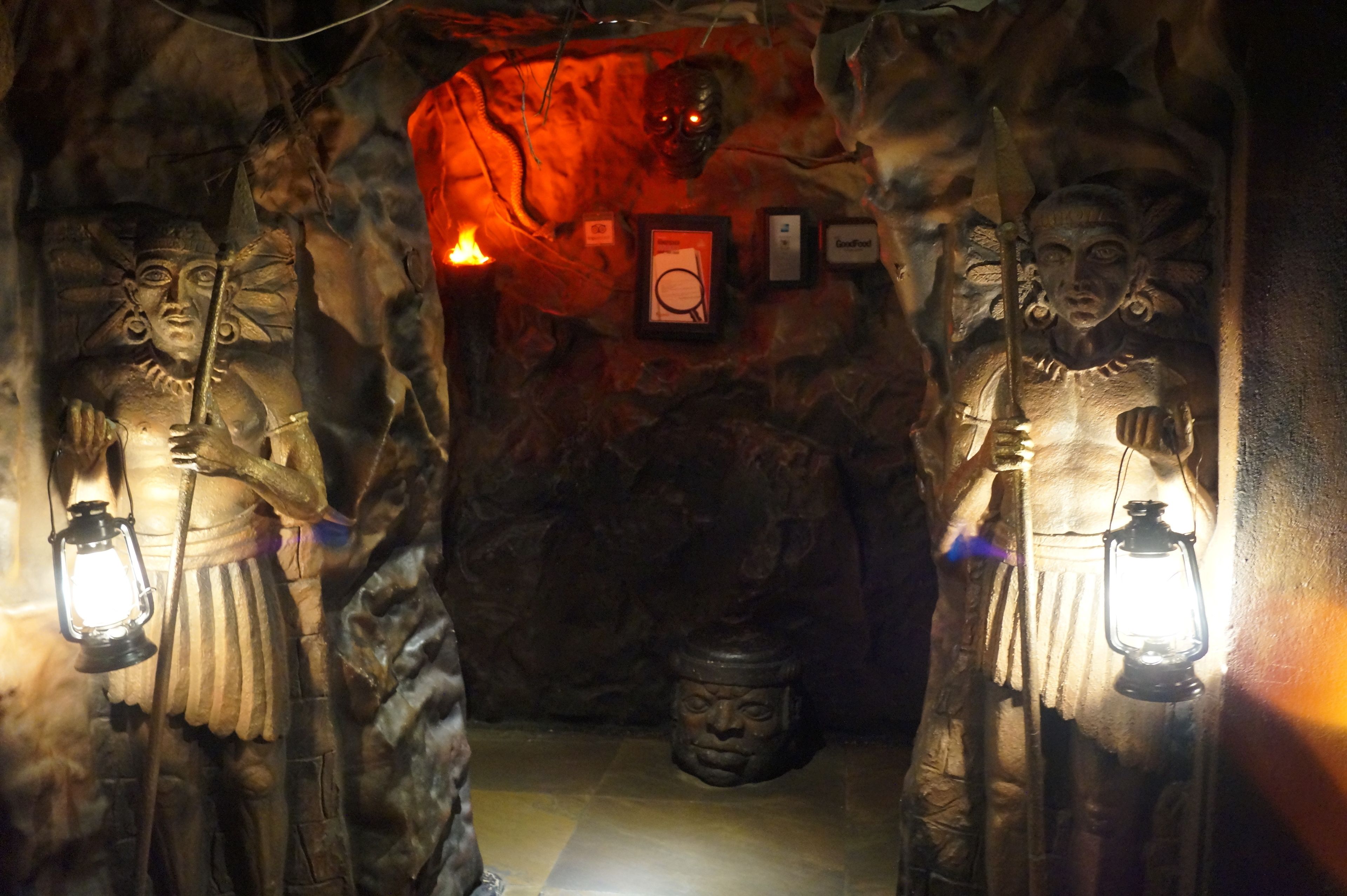 Une grotte faiblement éclairée, dont les parois sont ornées de sculptures représentant des personnages tenant des lanternes.