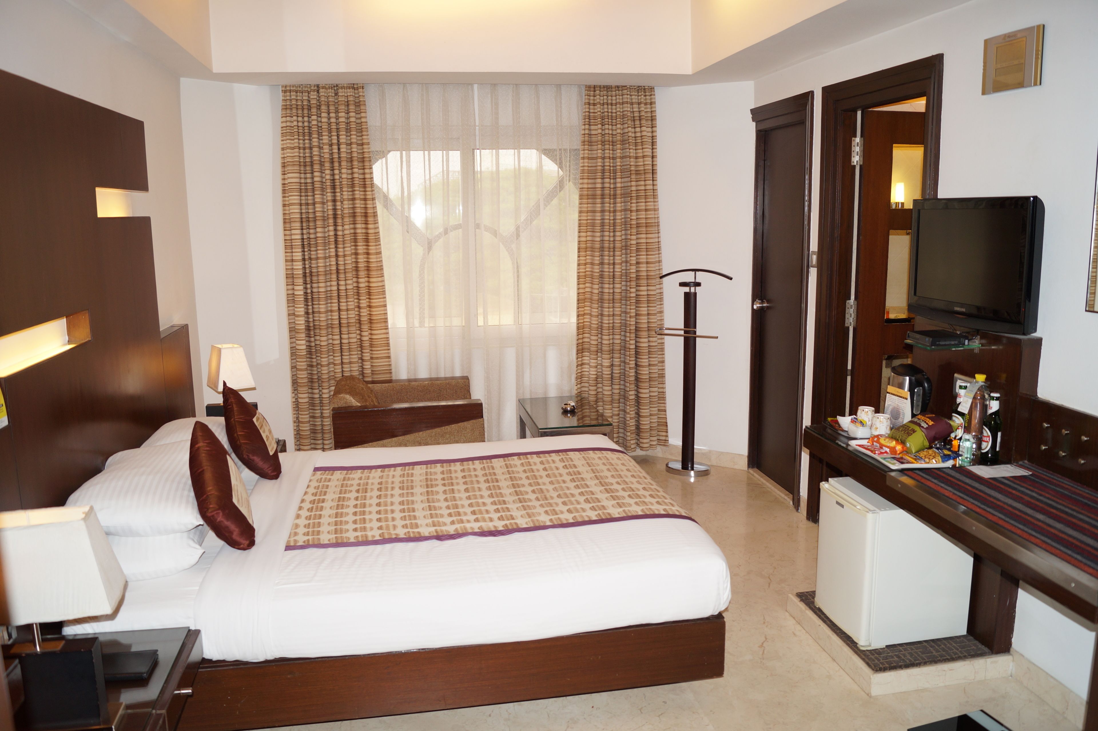 A hotel room with a bed, bedside table, lamp, television, and a small refrigerator.