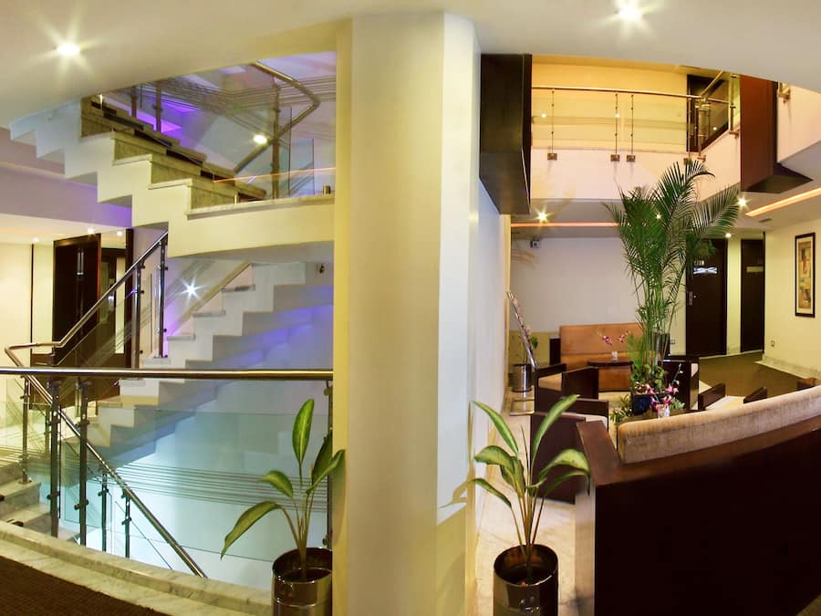A modern hotel lobby with a glass staircase, seating area, and artwork on the walls.