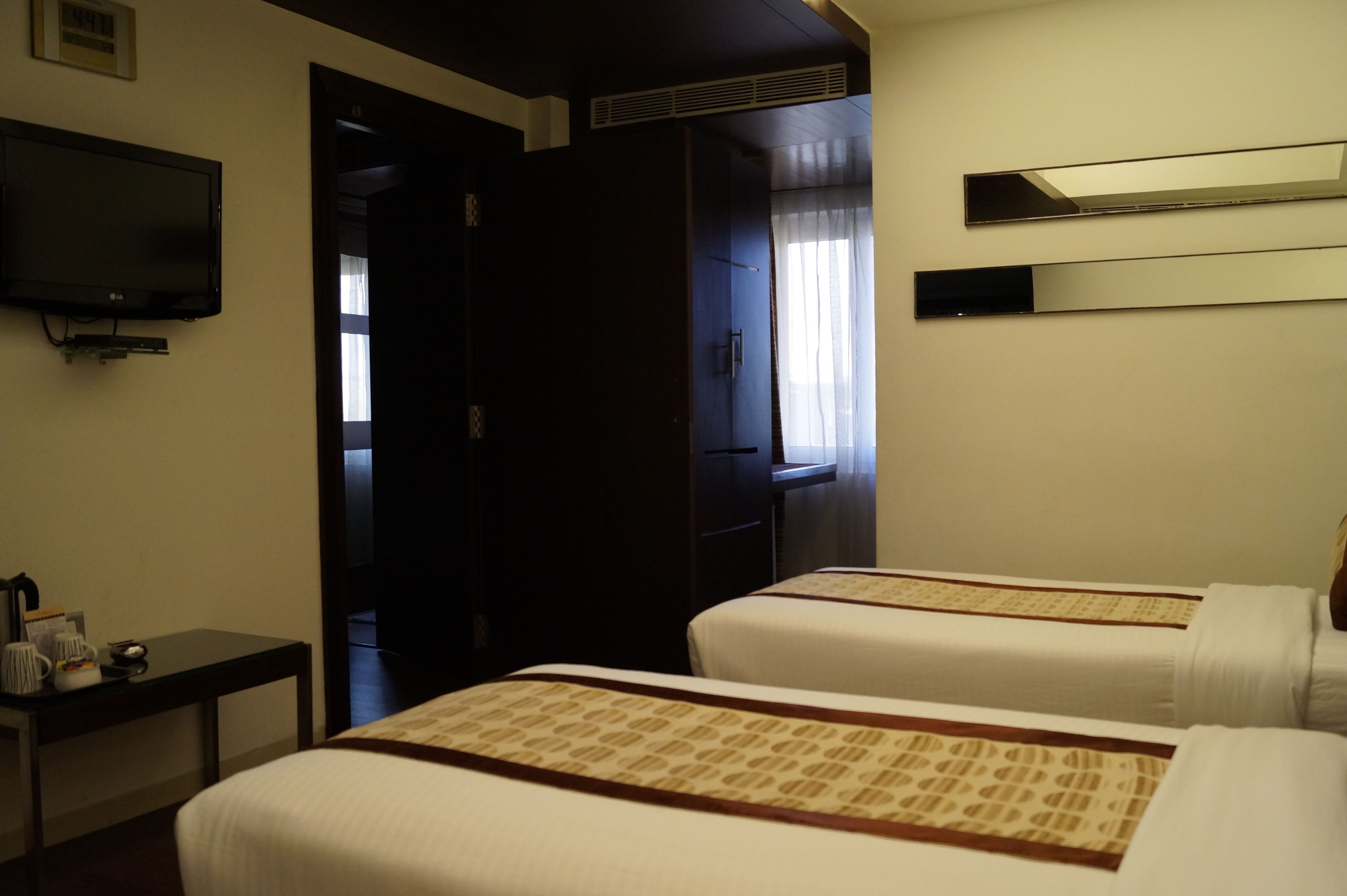 Ein Hotelzimmer mit zwei Betten, einem Fernseher, einem Schreibtisch und einem Kleiderschrank.