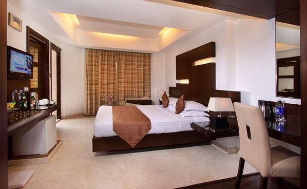 A hotel room with a bed, bedside table, lamp, chair, TV, and curtains. - The President Hotel (Bengaluru)