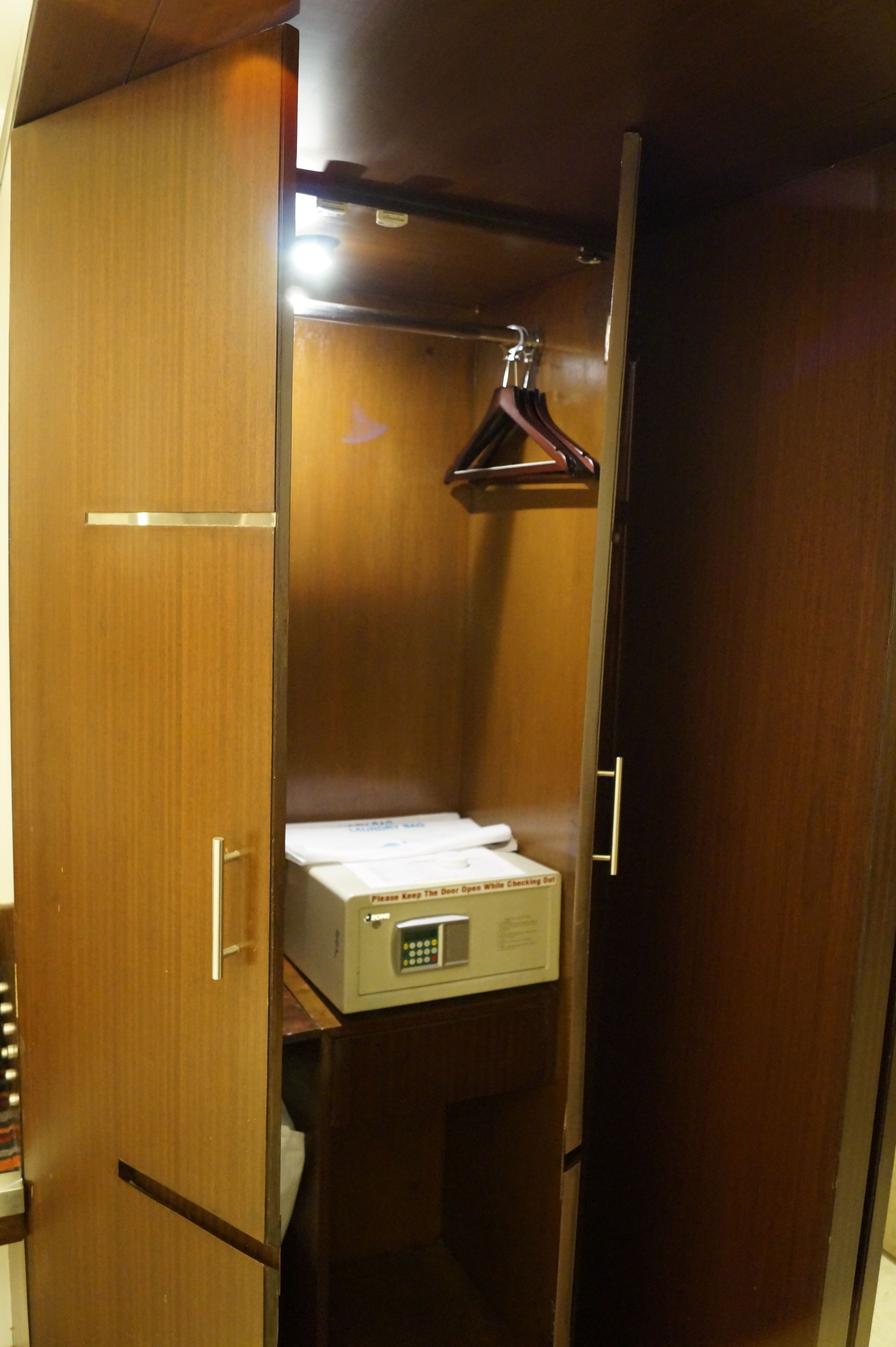 Un petit meuble-armoire en bois, doté d’un four à micro-ondes intégré et d’une tringle pour suspendre les vêtements.