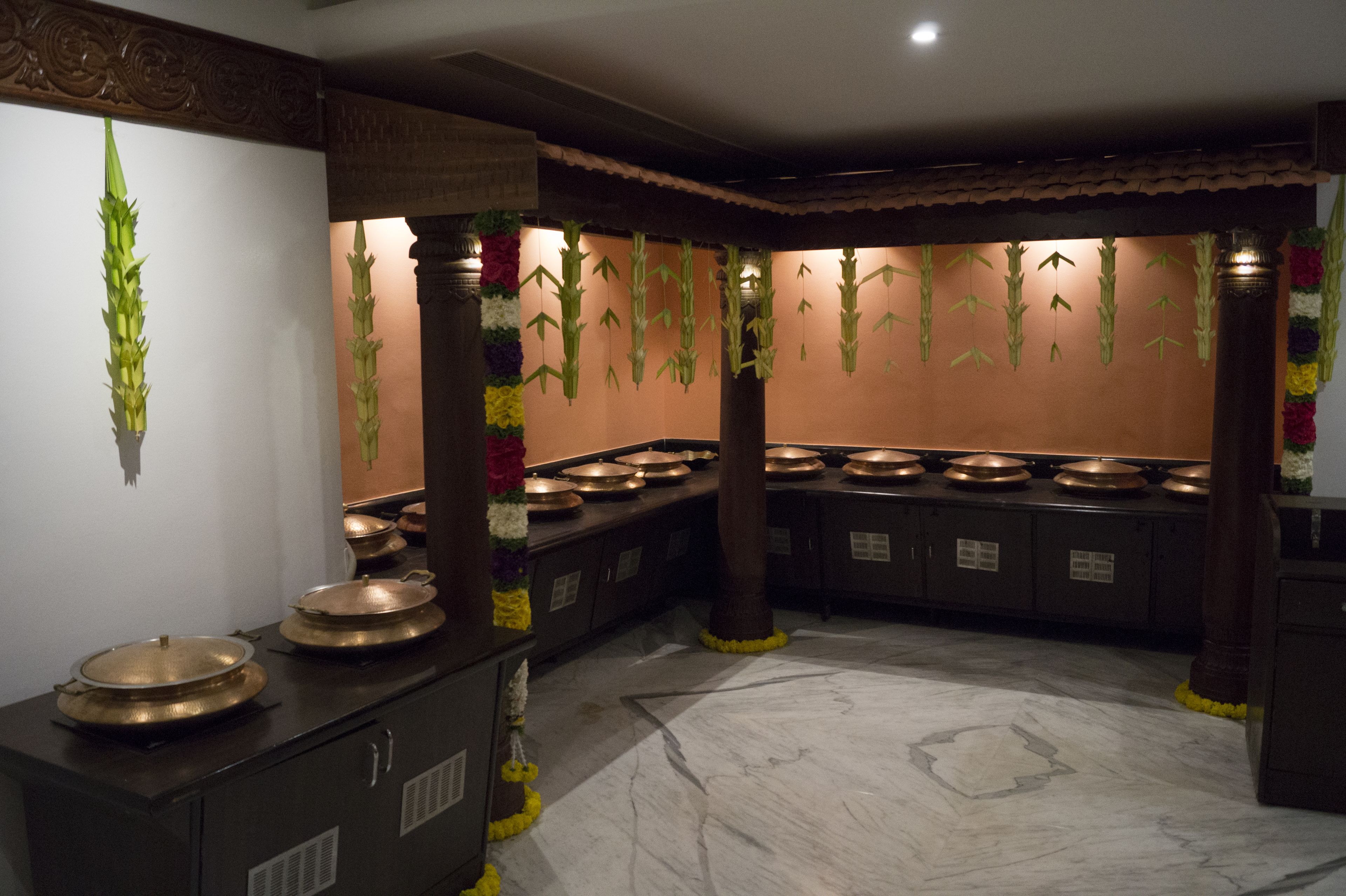 A kitchen with multiple copper pots on a counter, a marble floor, and decorative hanging plants.