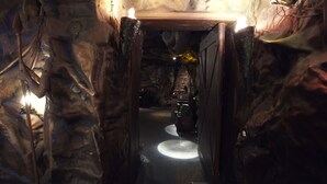 Un tunnel stretto e poco illuminato, con una porta di legno alla fine, che conduce a una piattaforma circolare con una fonte di luce.