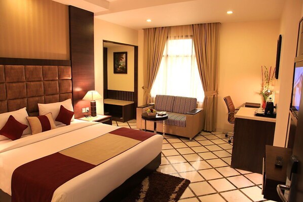 A hotel room with a large bed, a desk, a chair, a TV, and a window with curtains.