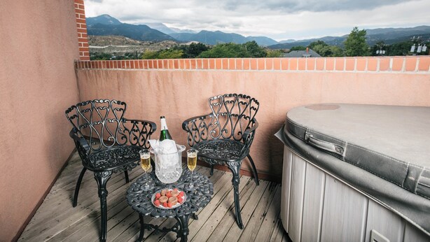 A balcony with two ornate metal chairs, a table with a bottle and glasses, and a hot tub. - Old Town GuestHouse B&B (Colorado Springs)