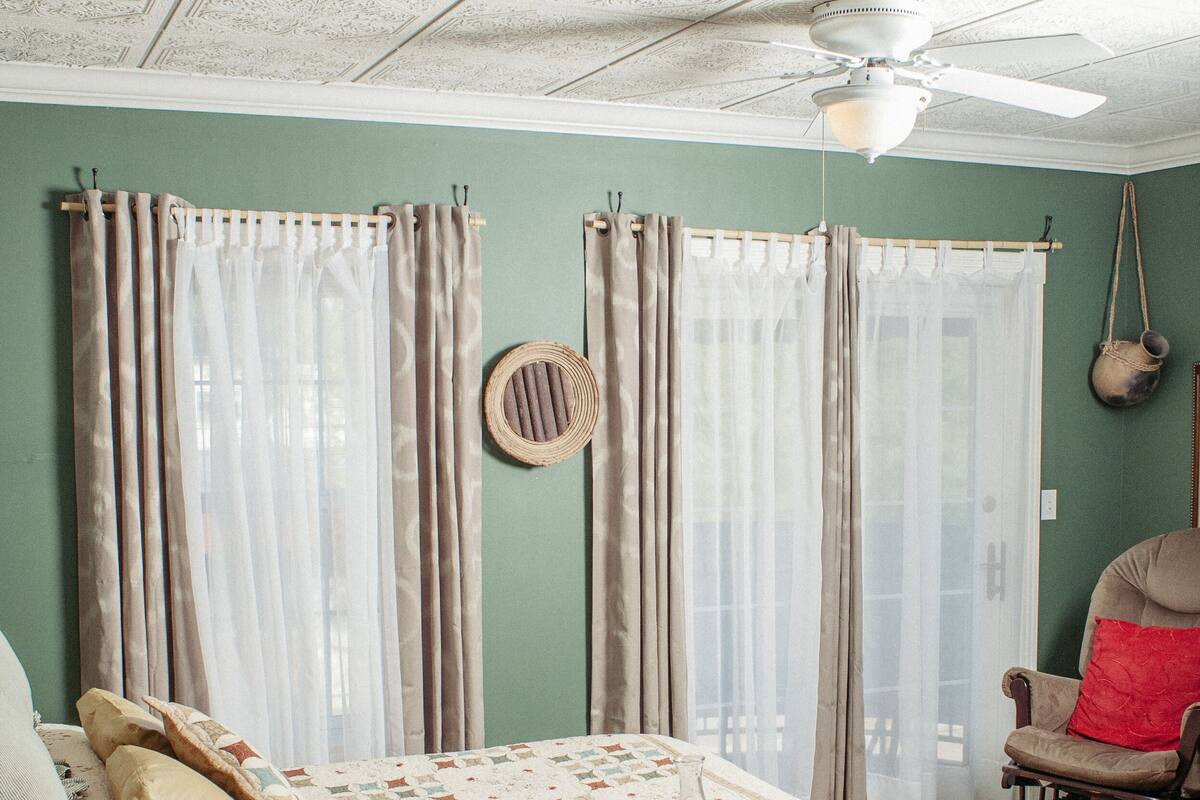 A cozy bedroom with a bed, curtains, a chair, and a quilted blanket.