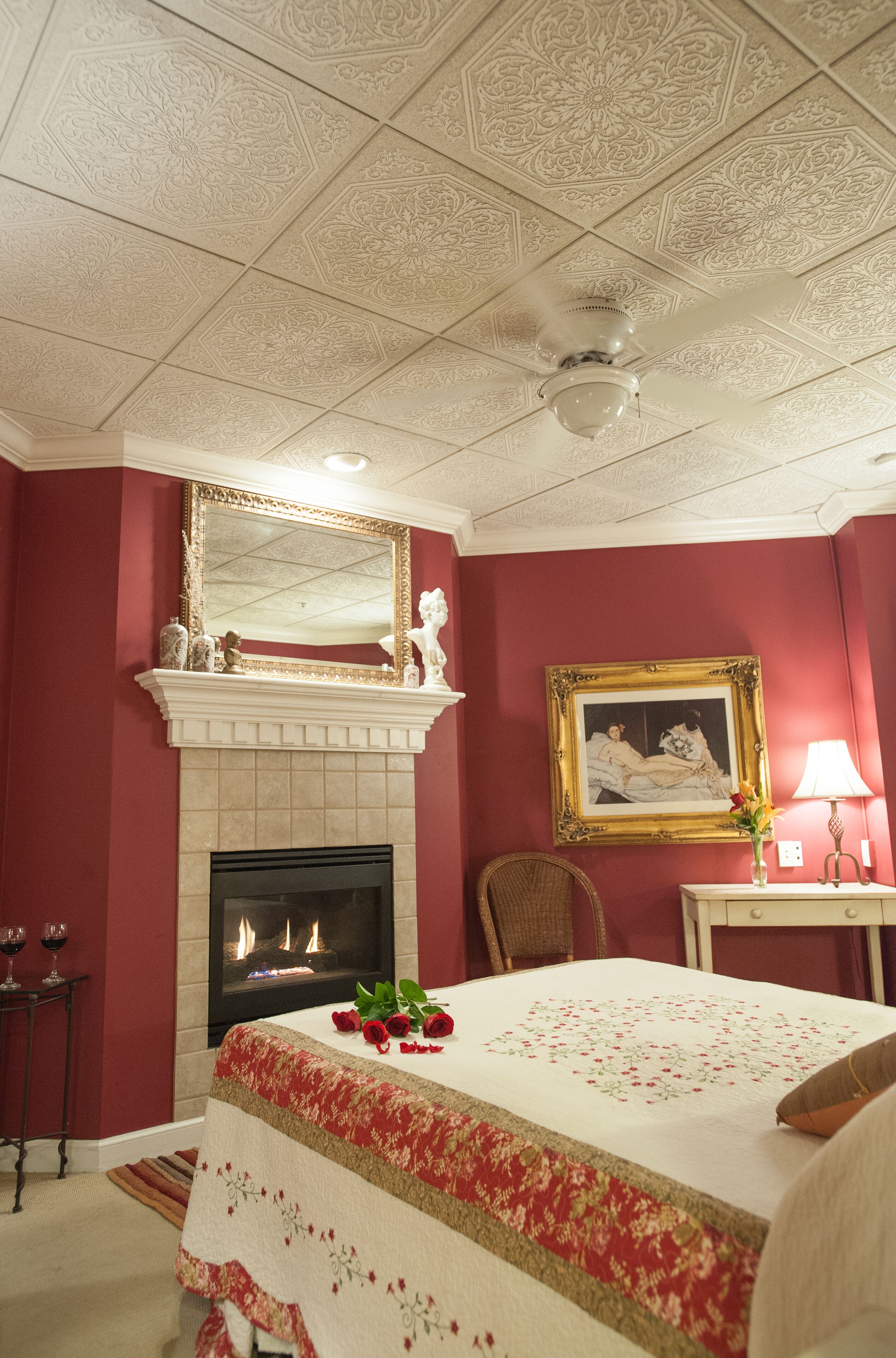 A room with a fireplace, a bed with a floral bedspread, a mirror above the fireplace, and a framed picture on the wall.