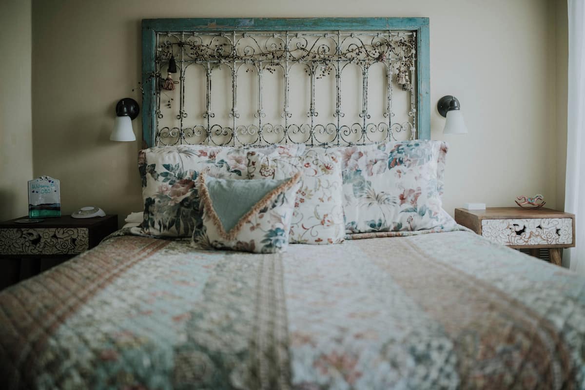 A bed with floral bedding, a decorative headboard, bedside lamps, and a small table with a decorative item.