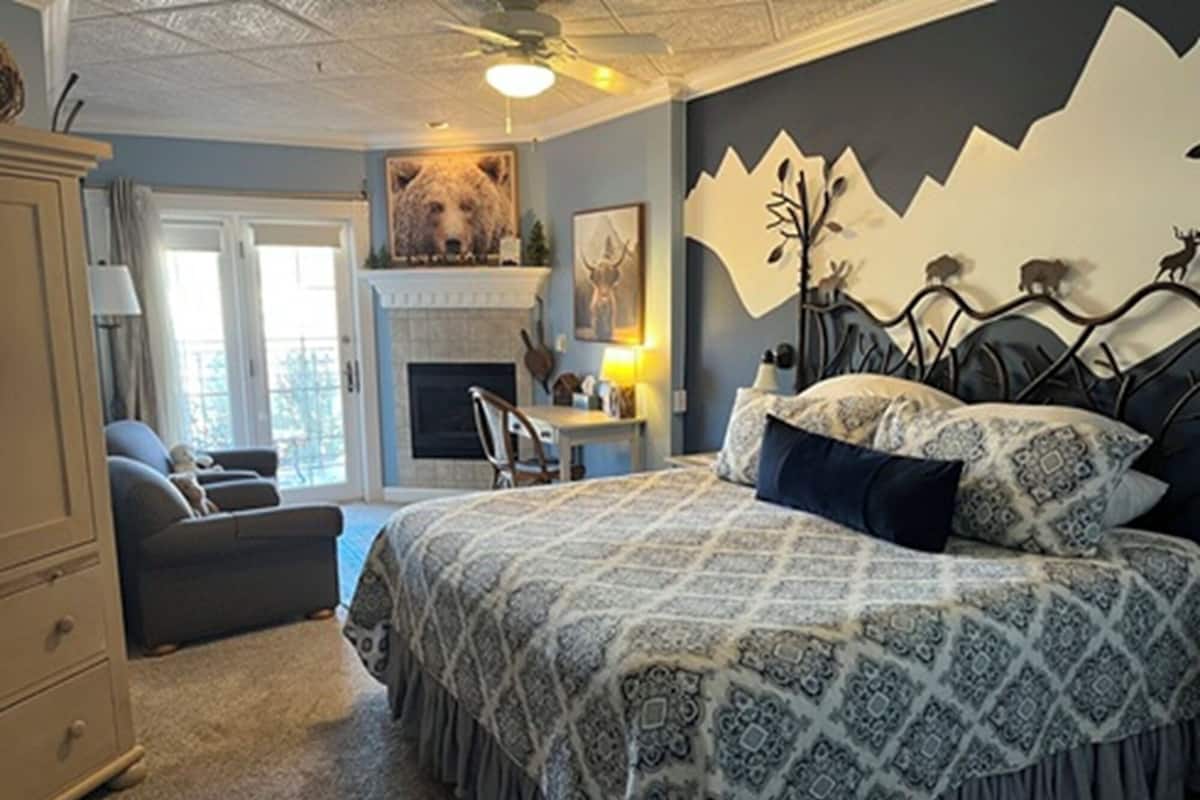 A bedroom with a large bed, a fireplace, a desk, and a chair.